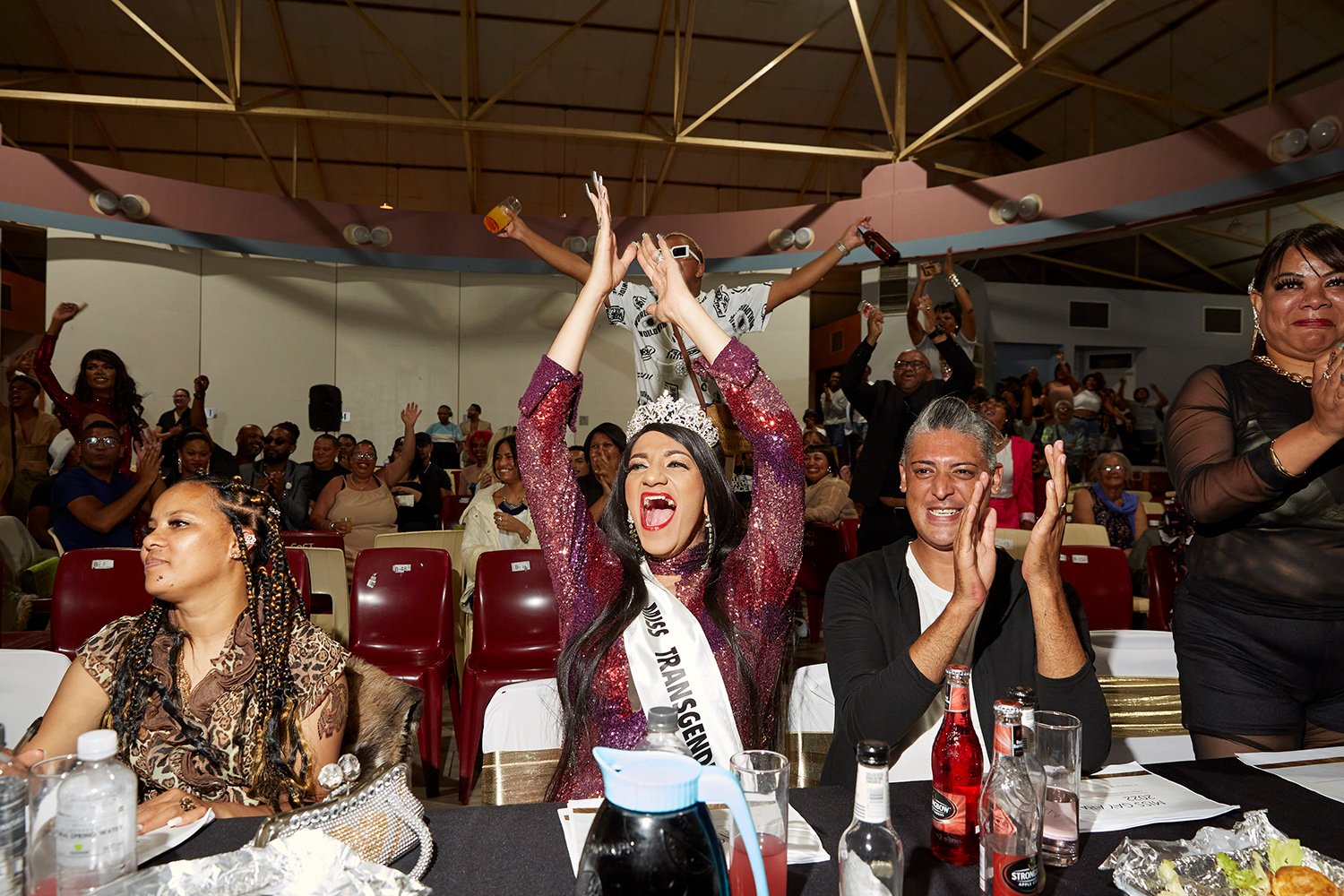  Taking a break from her duties as head judge, Chedino cheers as drag queen Emogen Moore performs during the Miss Gay Arabella beauty pageant, Grassy Park Civic Centre, Cape Town, 2022.  An experienced queen herself, Chedino is often asked to judge p