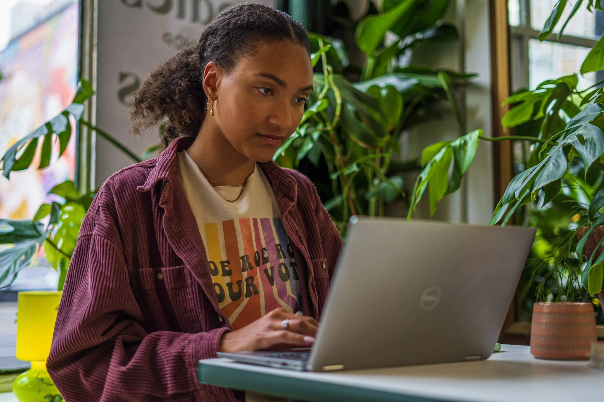 Young woman using a laptop at a desk surrounded by green plants.