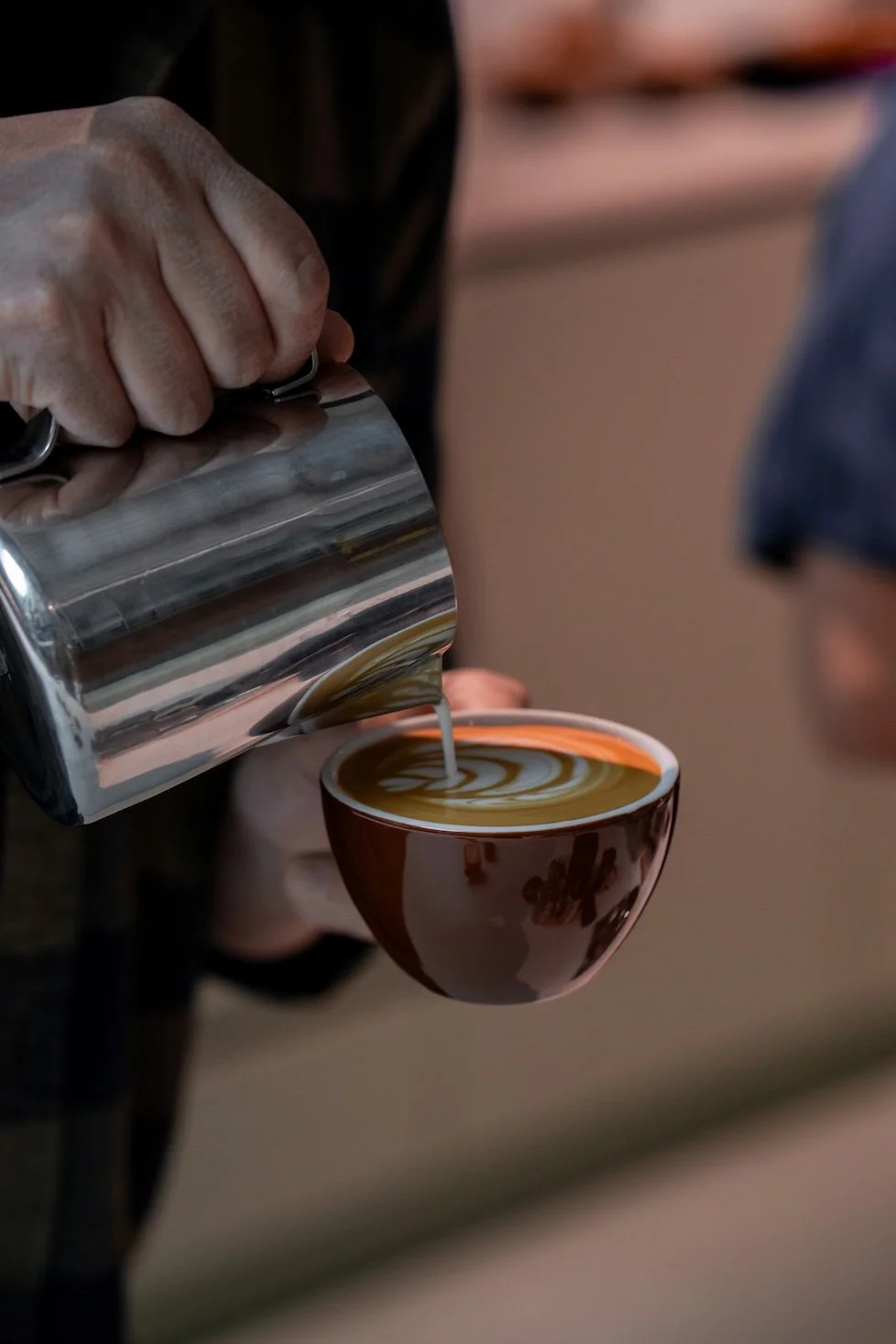 Close-up of a barista pouring textured milk into espresso to create latte art.