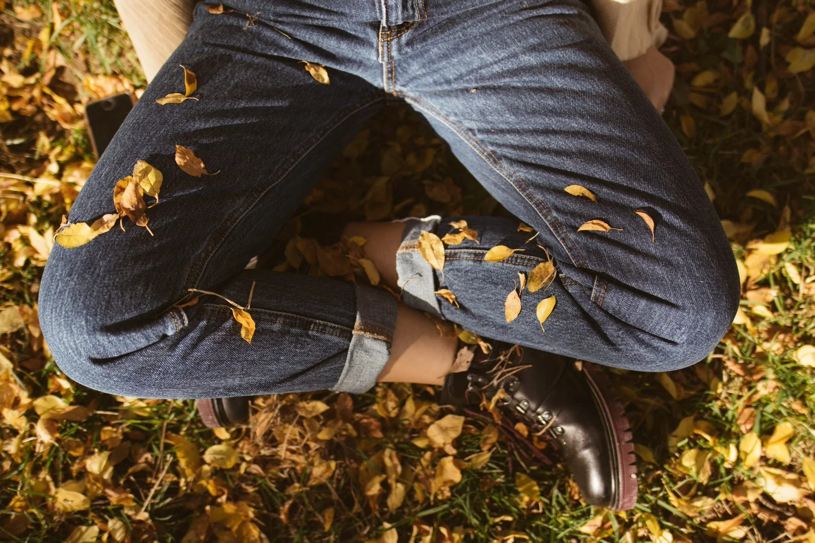 A person meditating with crossed legs, sitting in the yellow leaves on a ground