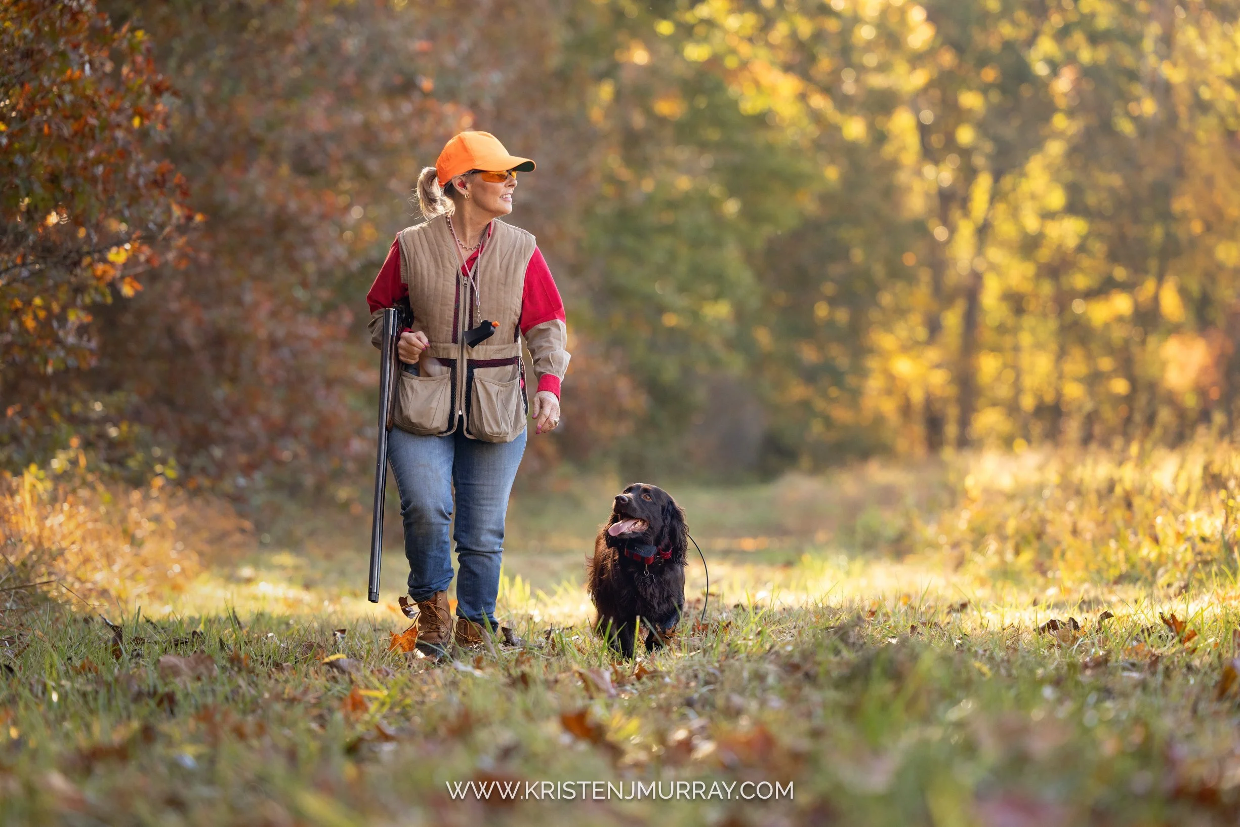 A woman walking with her black dog in a park during autumn, with colorful fall foliage and a sunlit path. Woman with bird dog - Upland Hunting in Virginia