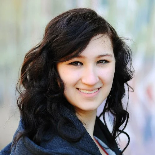 A young woman with dark wavy hair smiling outdoors.