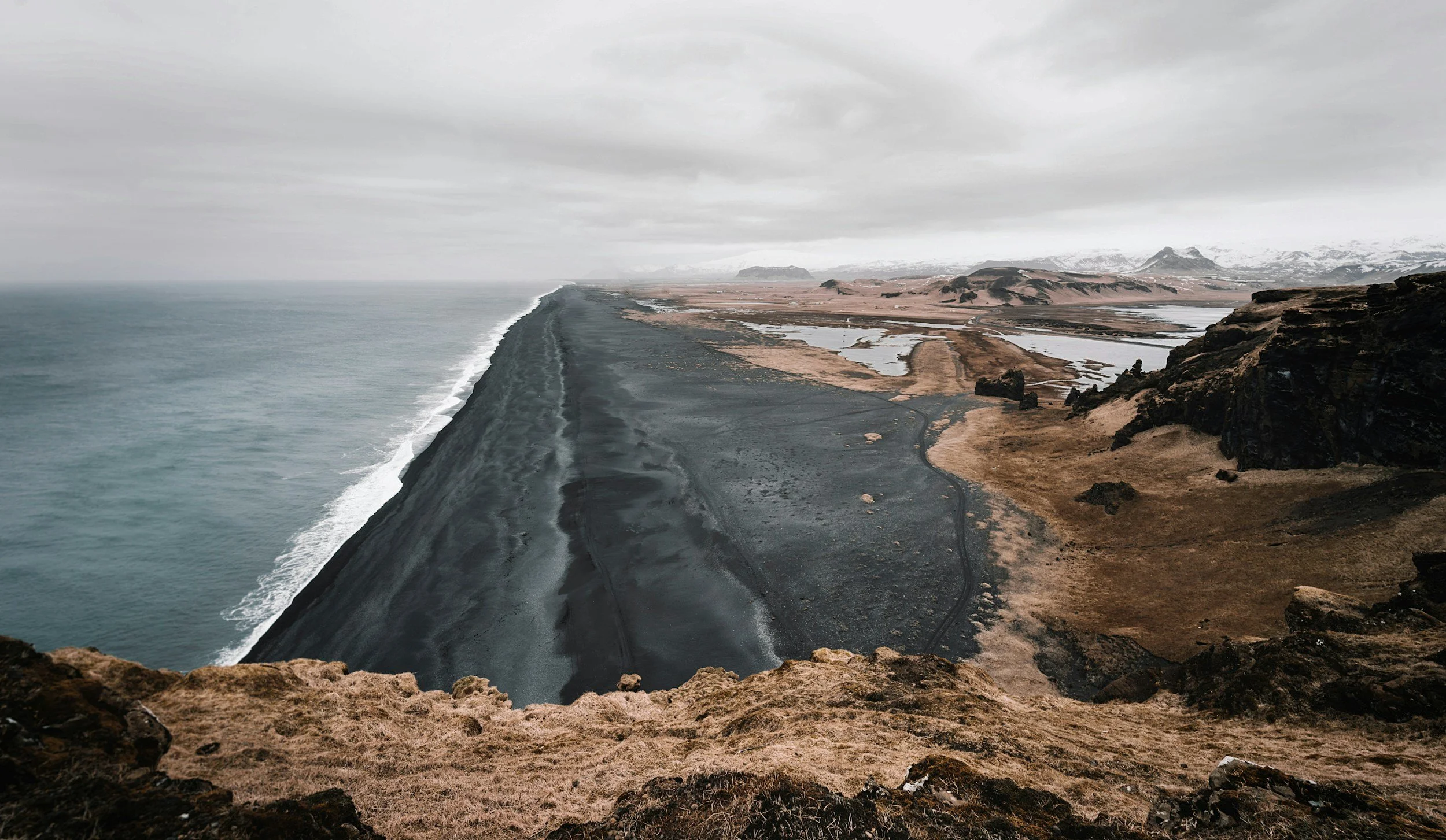 Dramatic landscape of a volcanic ash road along the coast with a rugged terrain and a cloudy sky.