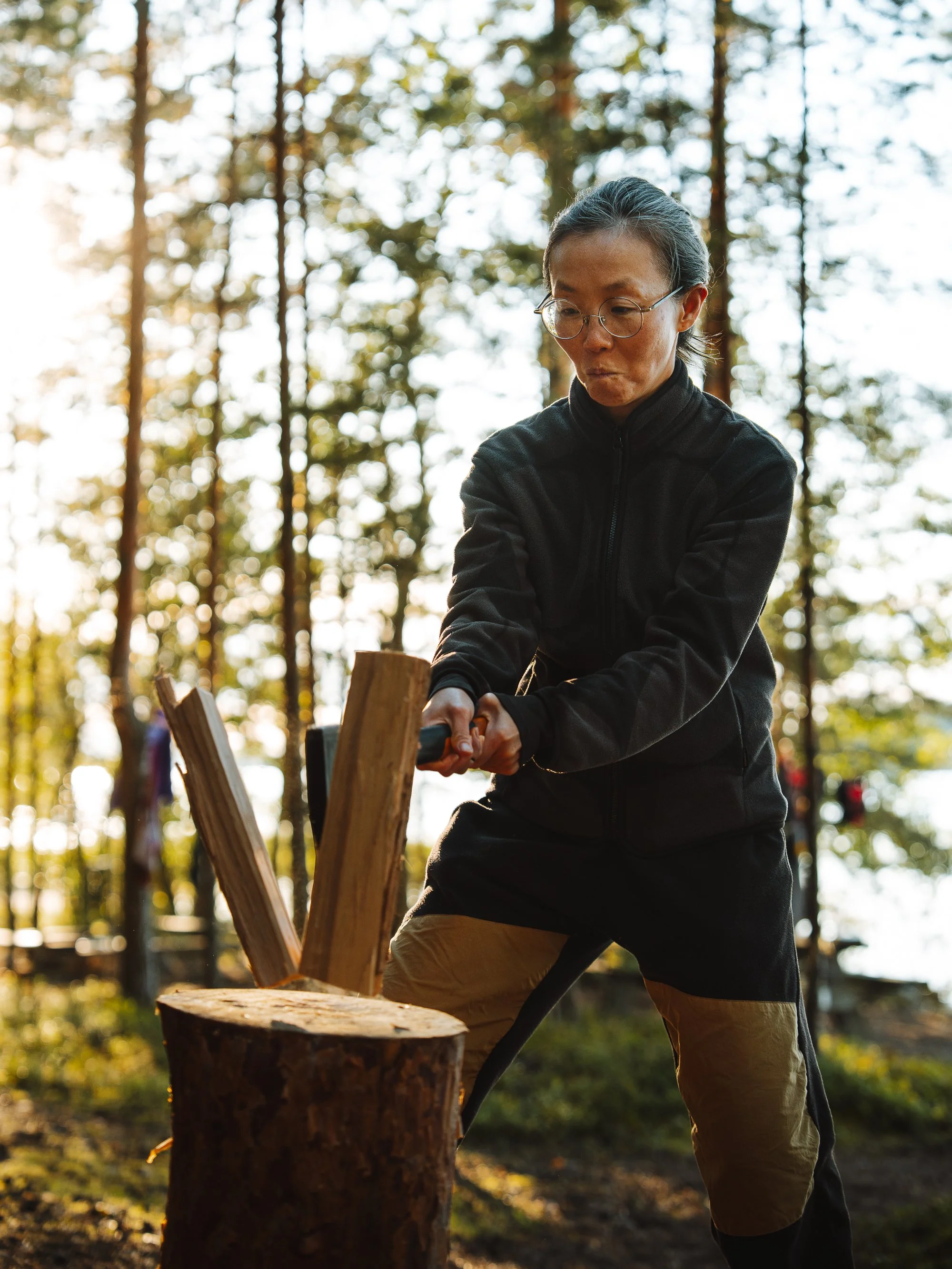 A person chopping wood with an axe in a forest during sunset.