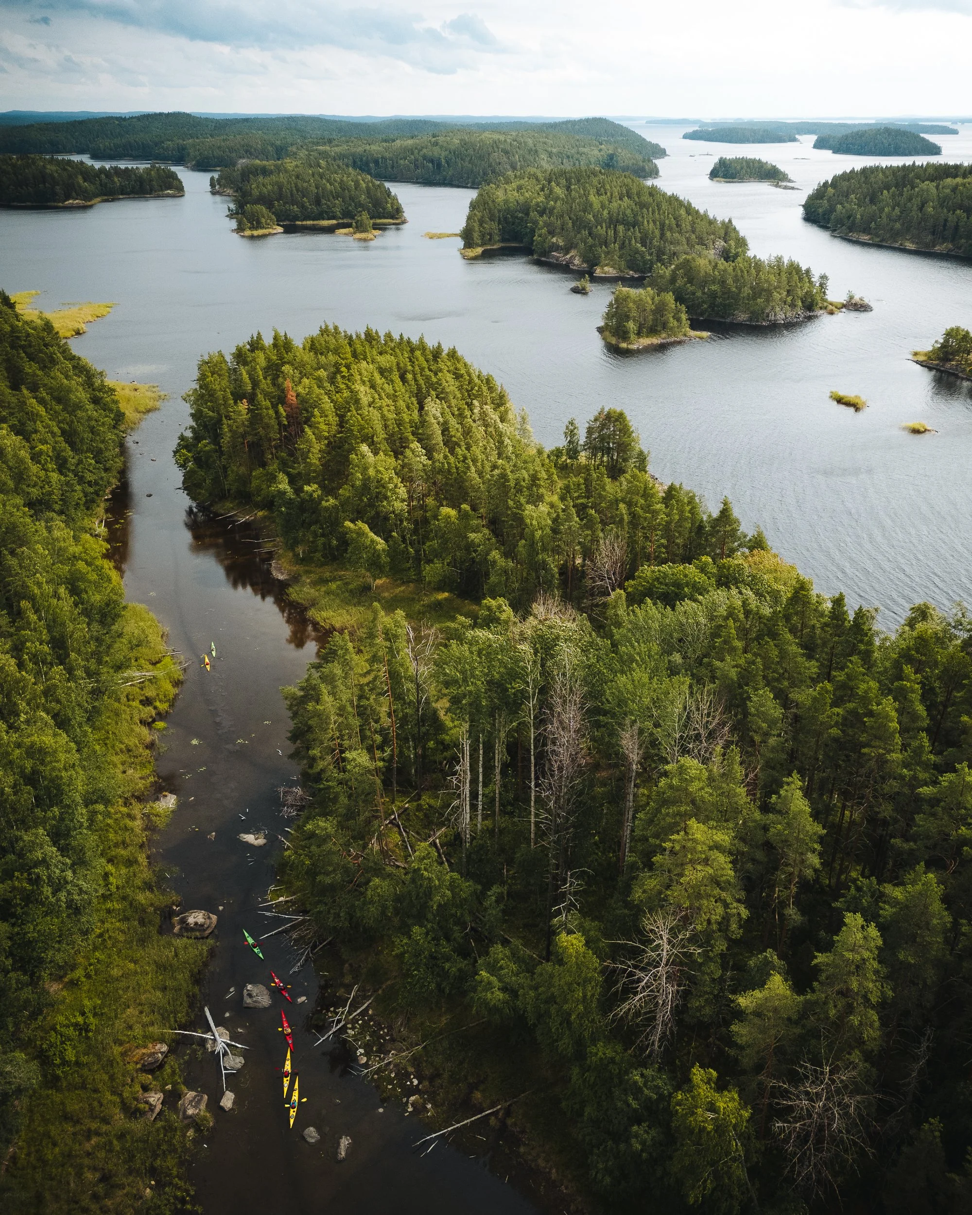 Aerial view of a river with multiple small islands, trees, and kayakers paddling in the water.
