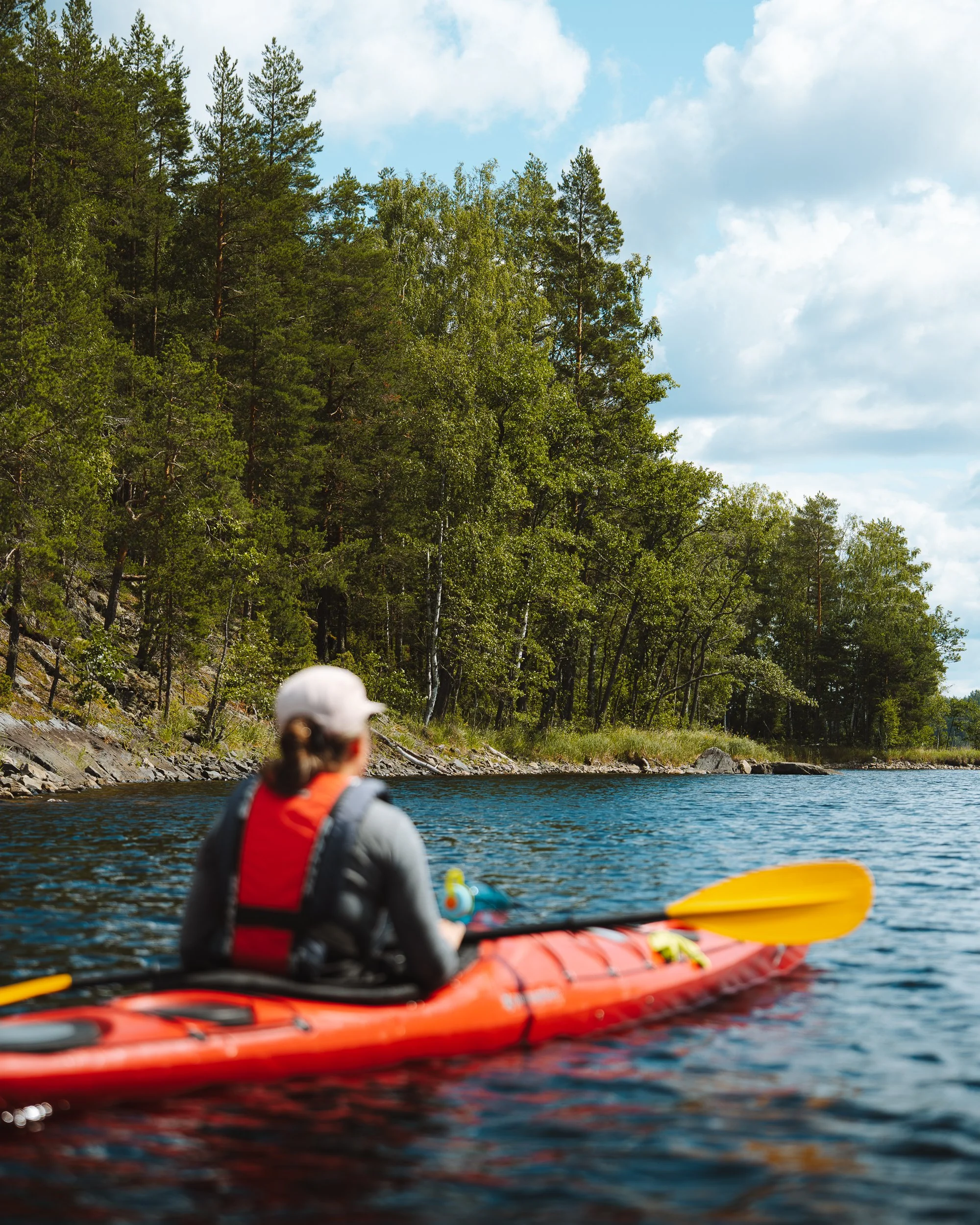 Person kayaking on a river surrounded by trees and a cloudy sky.