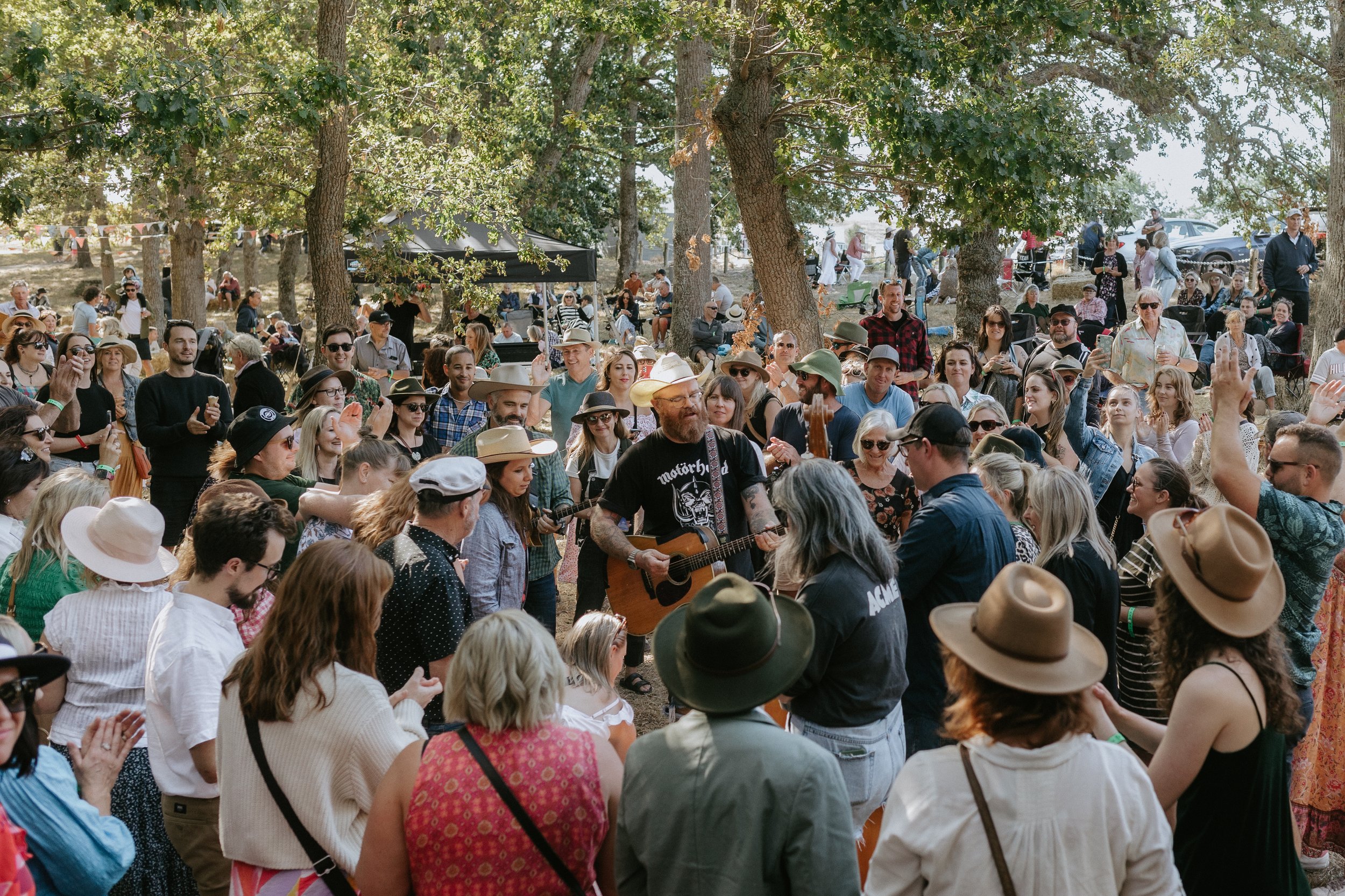 Guitarist performing among a festival crowd beneath trees