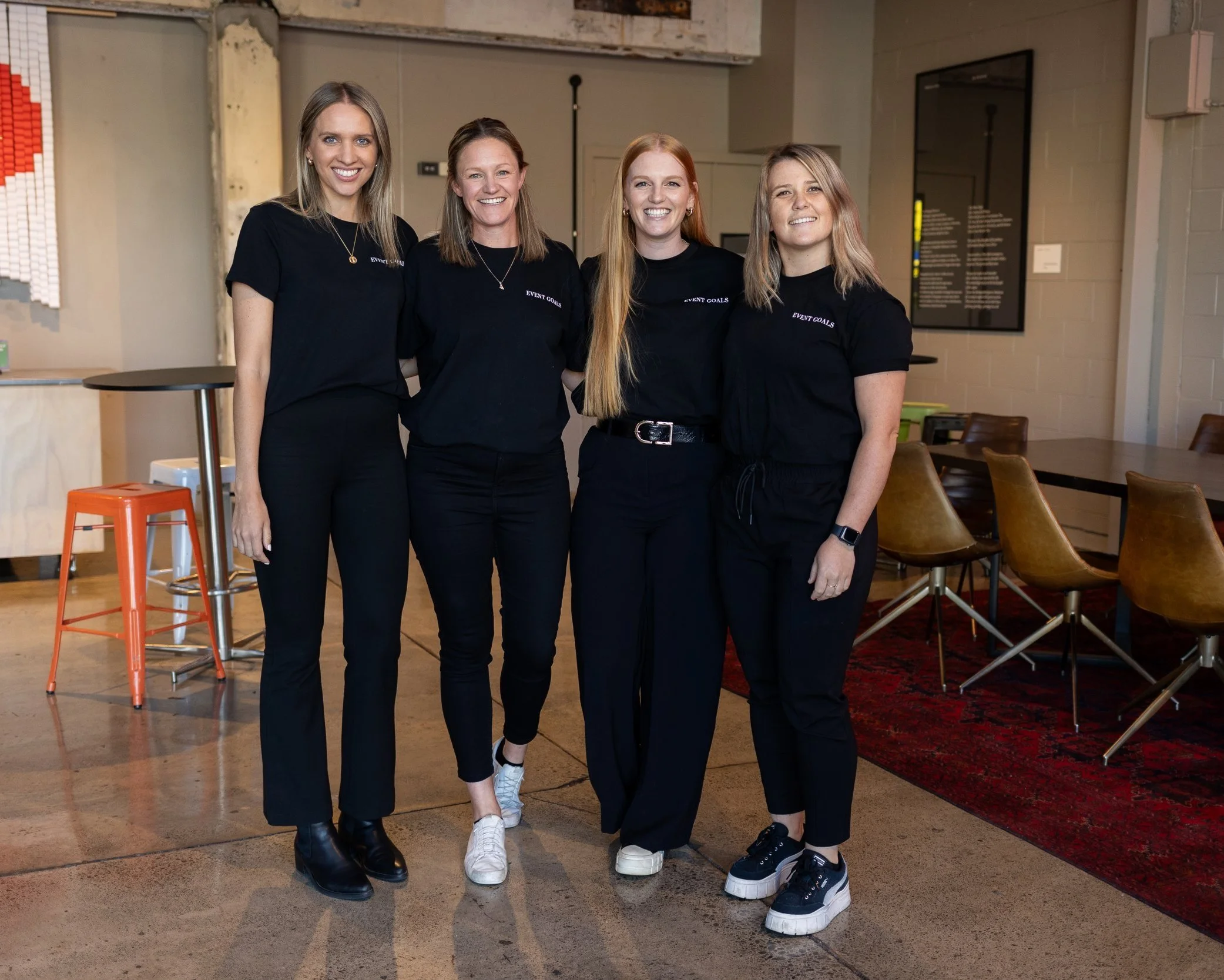 Four Event Goals team members in black branded shirts at an event venue