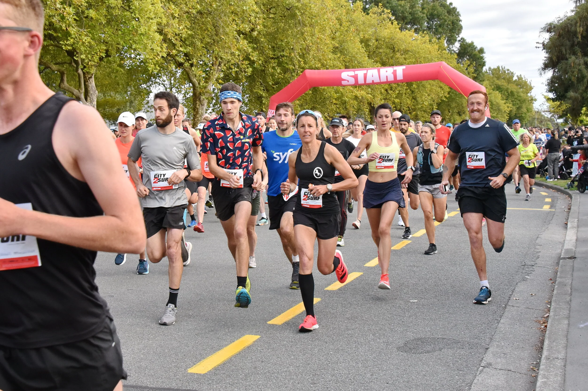 City2Surf runners passing the start arch on a tree-lined road