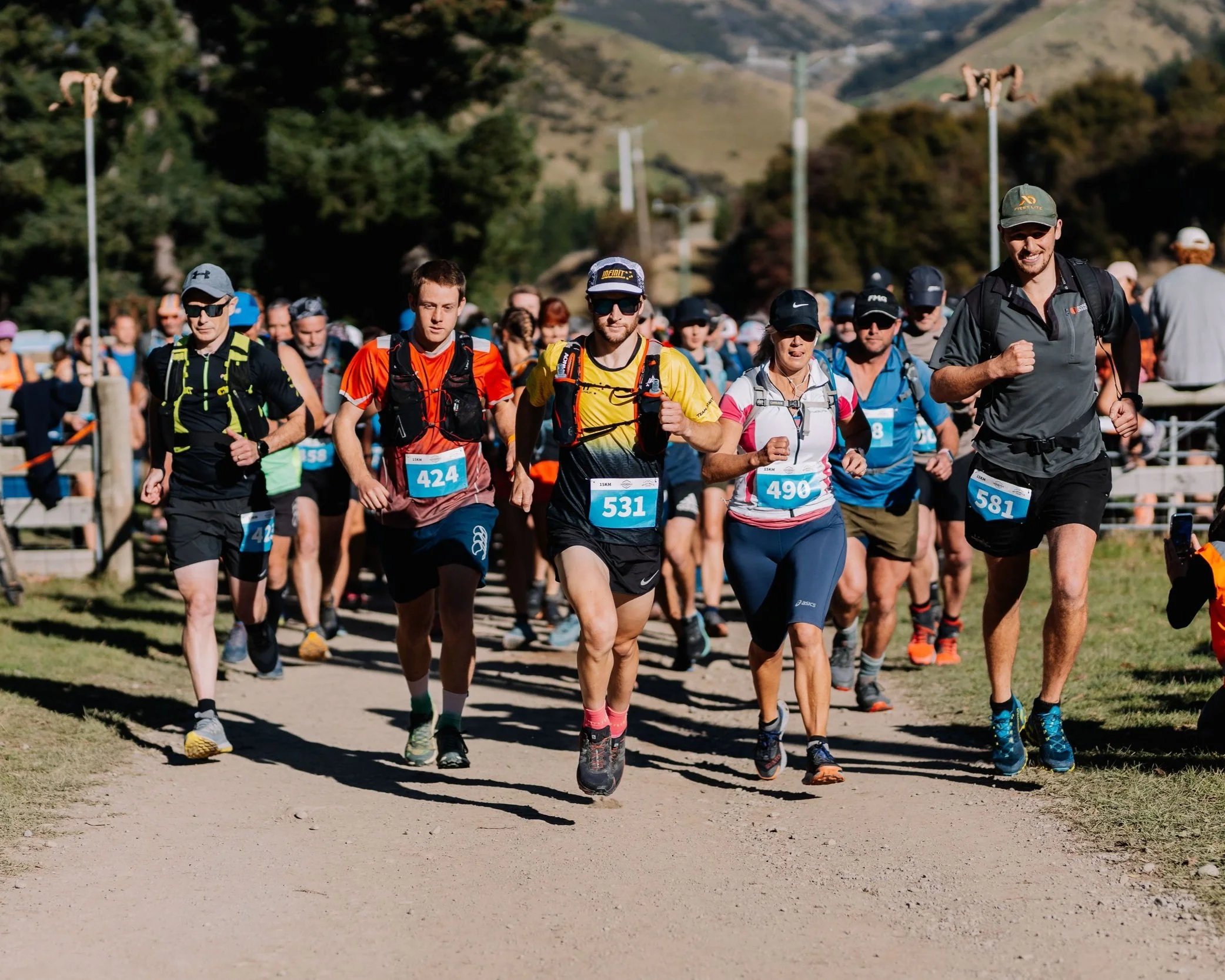 Trail race participants wearing numbered bibs running along a gravel track