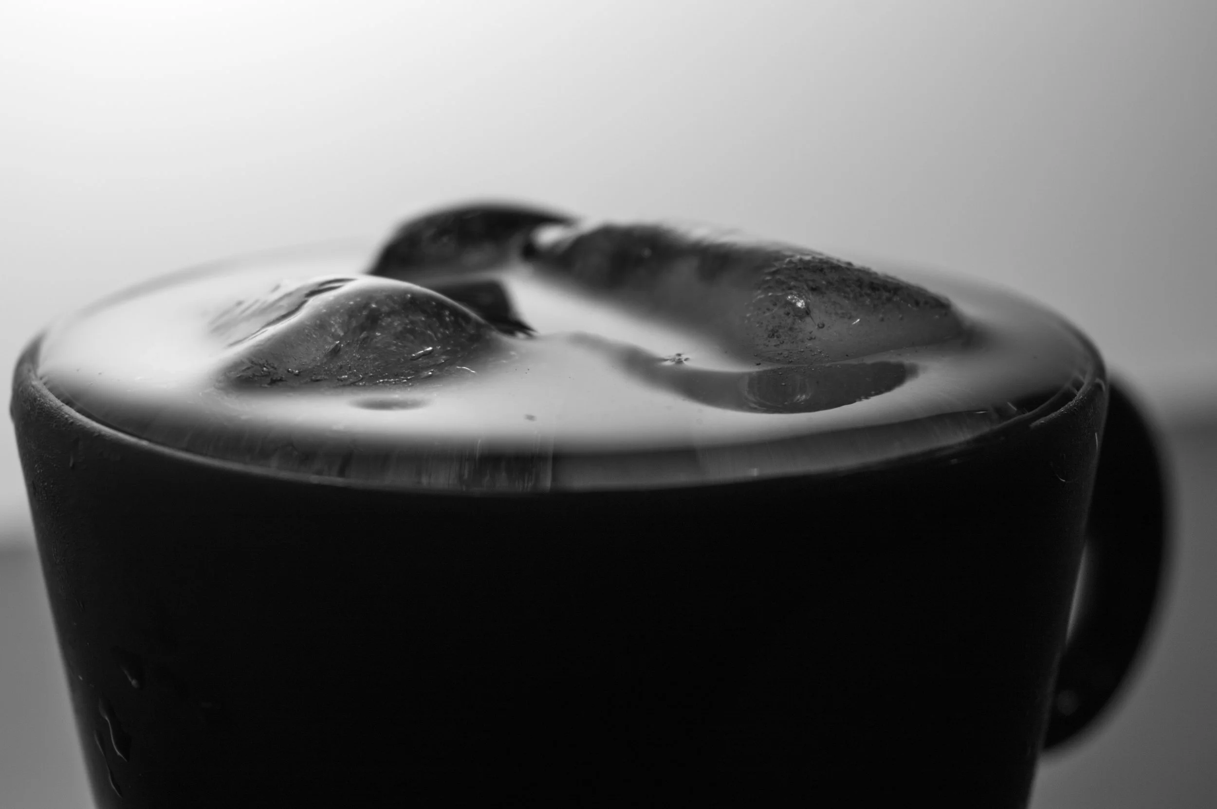 Close-up of a glass filled with a dark, liquid beverage and ice cubes, with a smooth surface and slightly rounded top.
