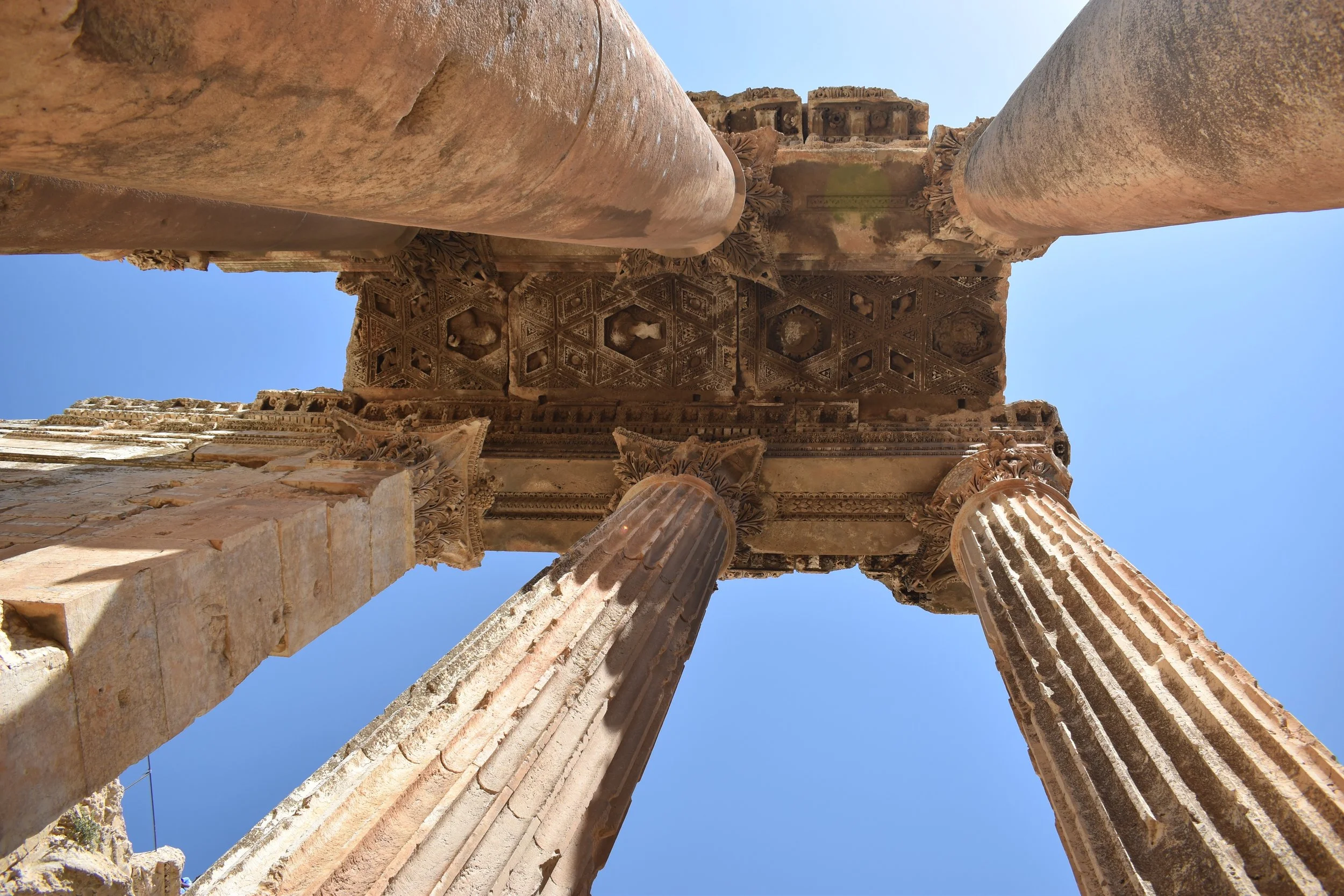 Ancient Roman ruins with tall, decorated columns and intricate stone carvings under a clear blue sky.
