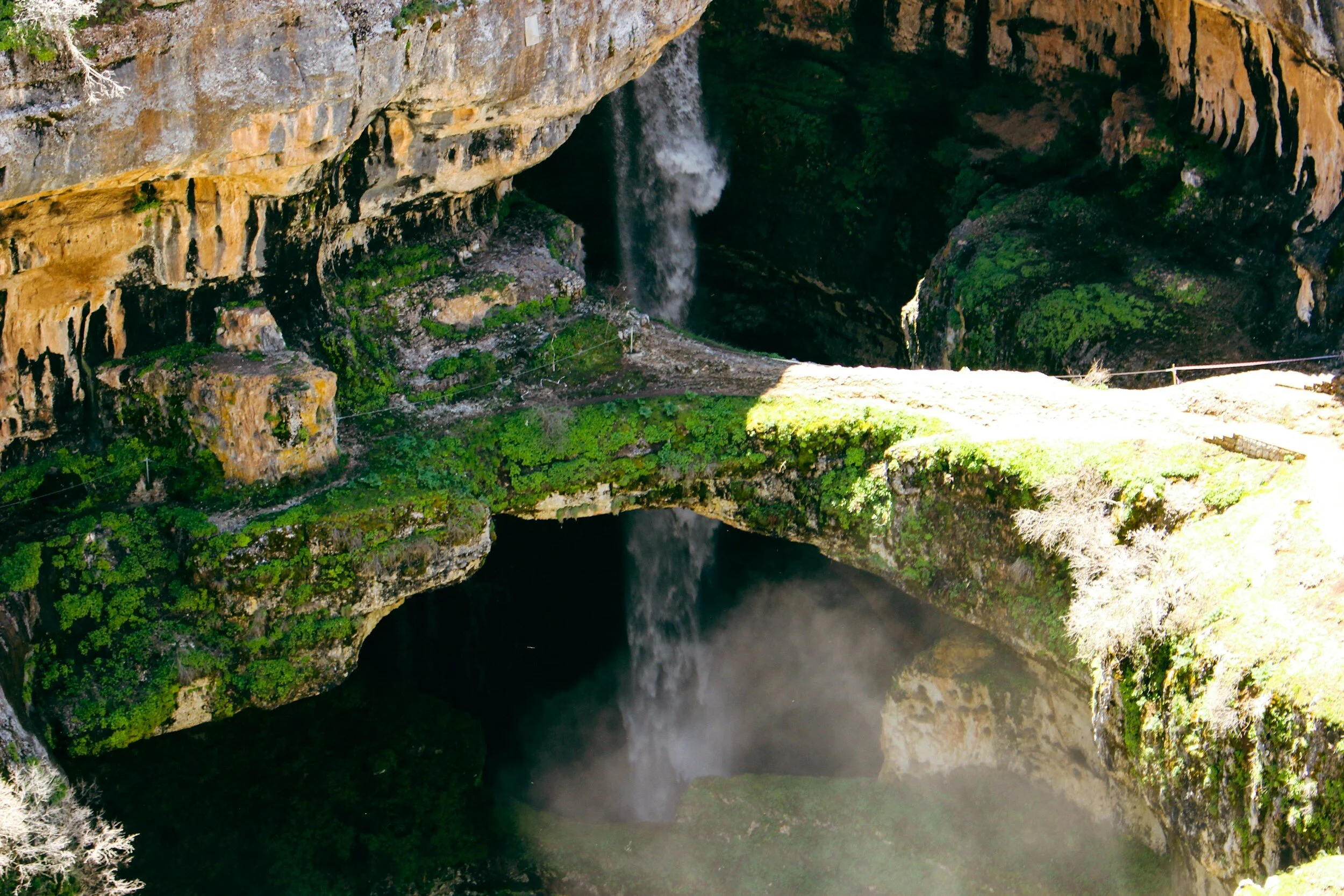 A natural landscape with a waterfall cascading into a deep canyon, surrounded by moss-covered rocks and lush green vegetation.