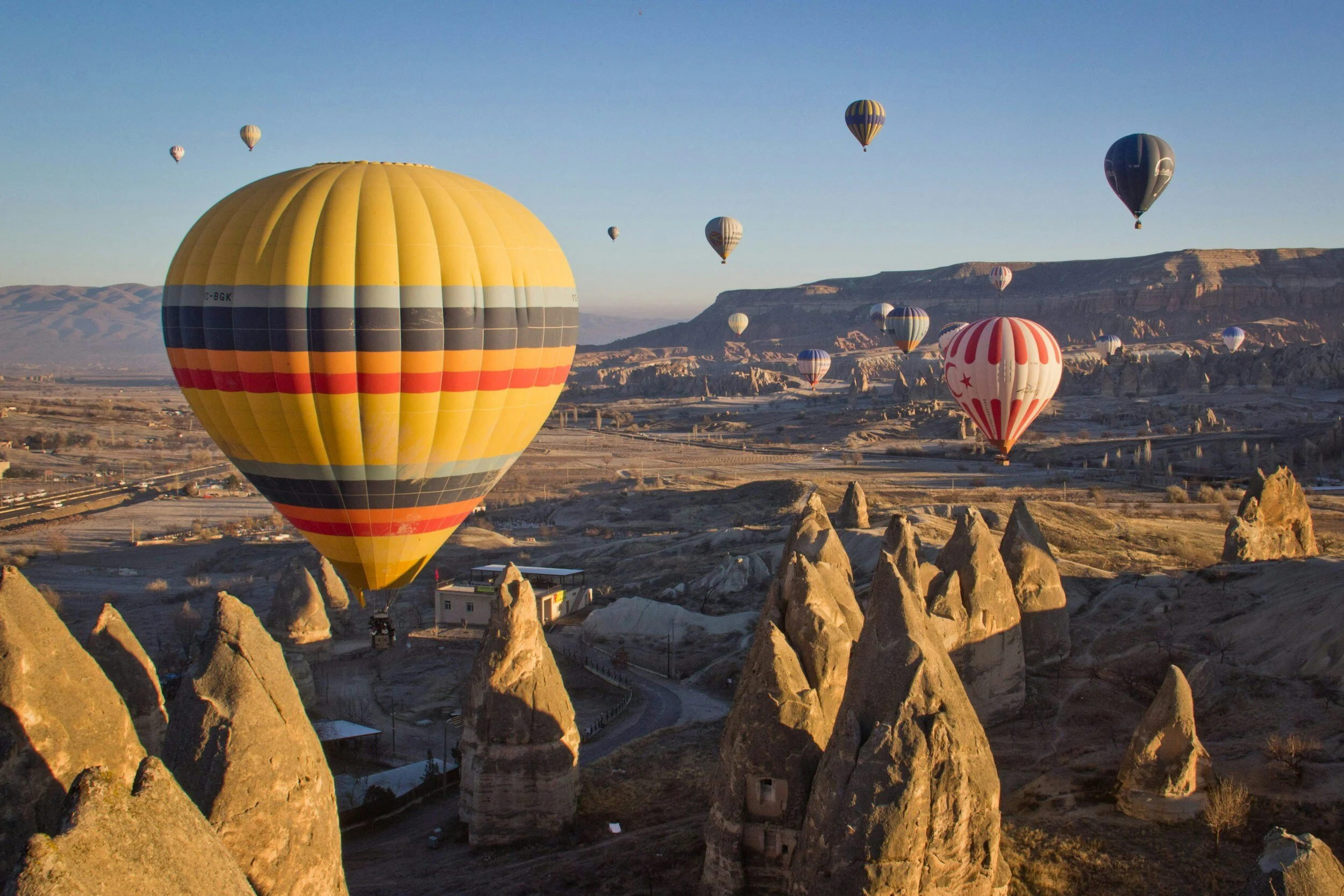 Multiple hot air balloons floating over a rocky landscape with unique tall rock formations during sunrise or sunset.