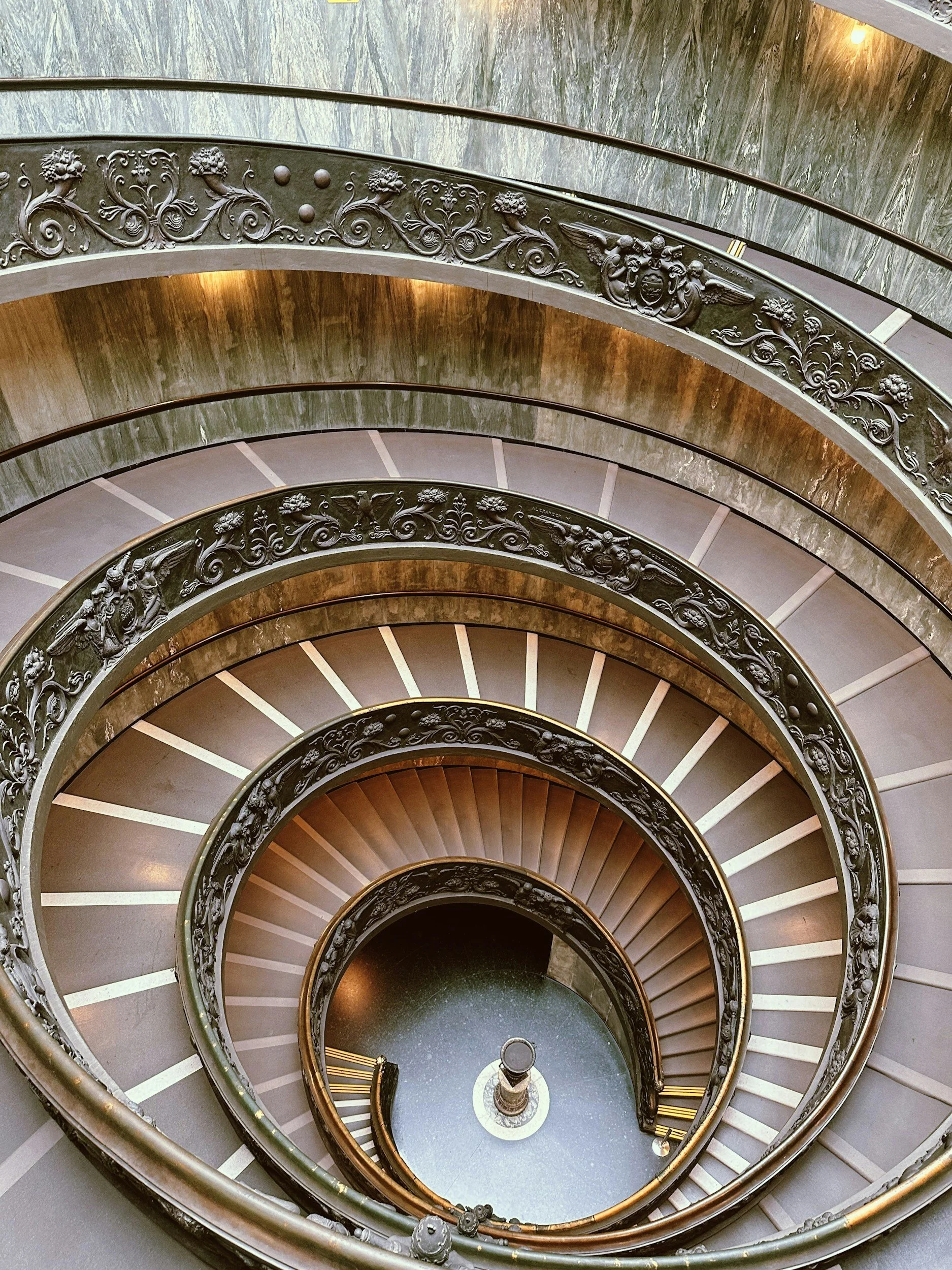 View of a spiral staircase with ornate metal railing and decorative details, photographed from above.