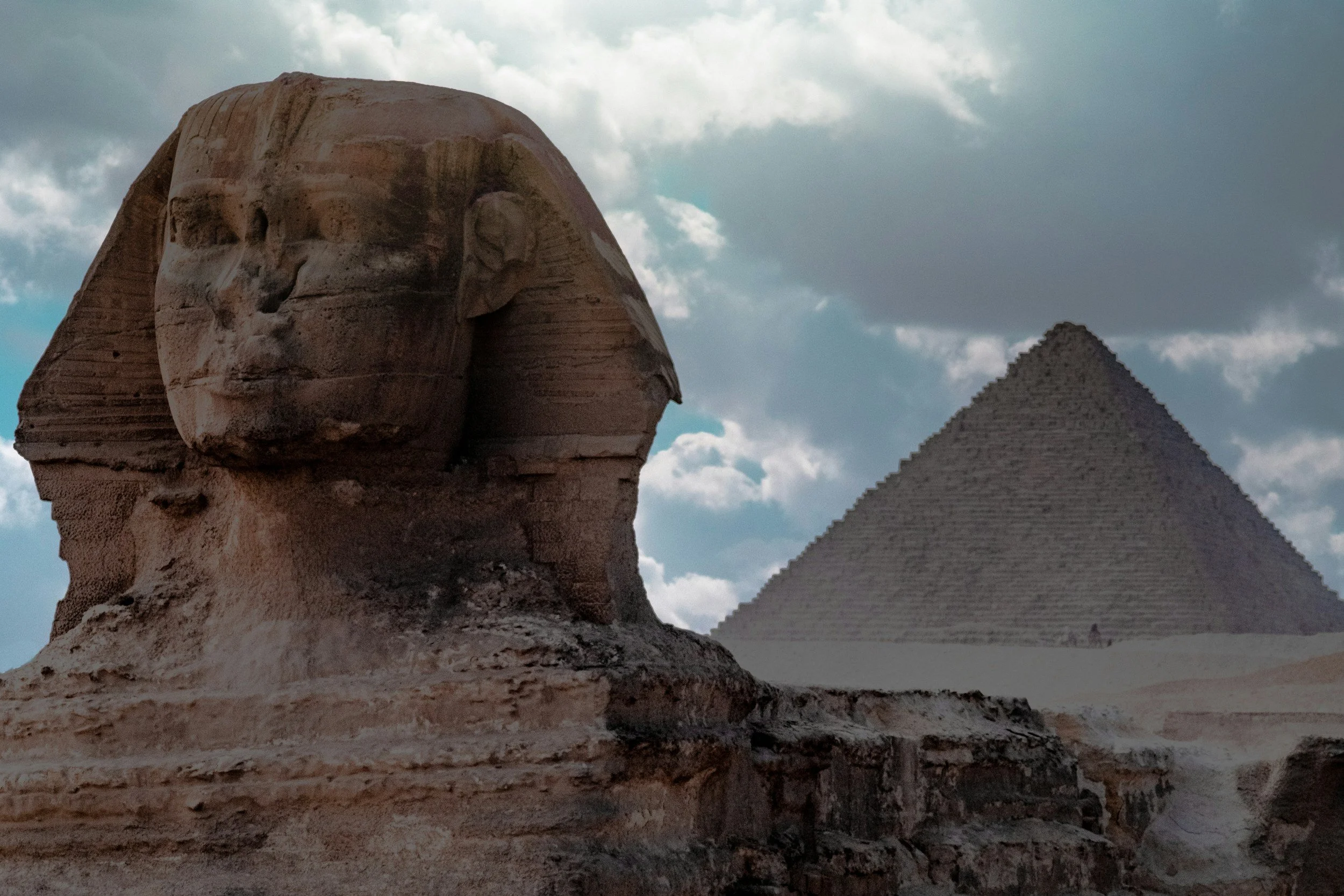 Ancient Egyptian monuments, including the Great Sphinx of Giza with a lion's body and a human head, and the Great Pyramid of Giza in the background under a cloudy sky.