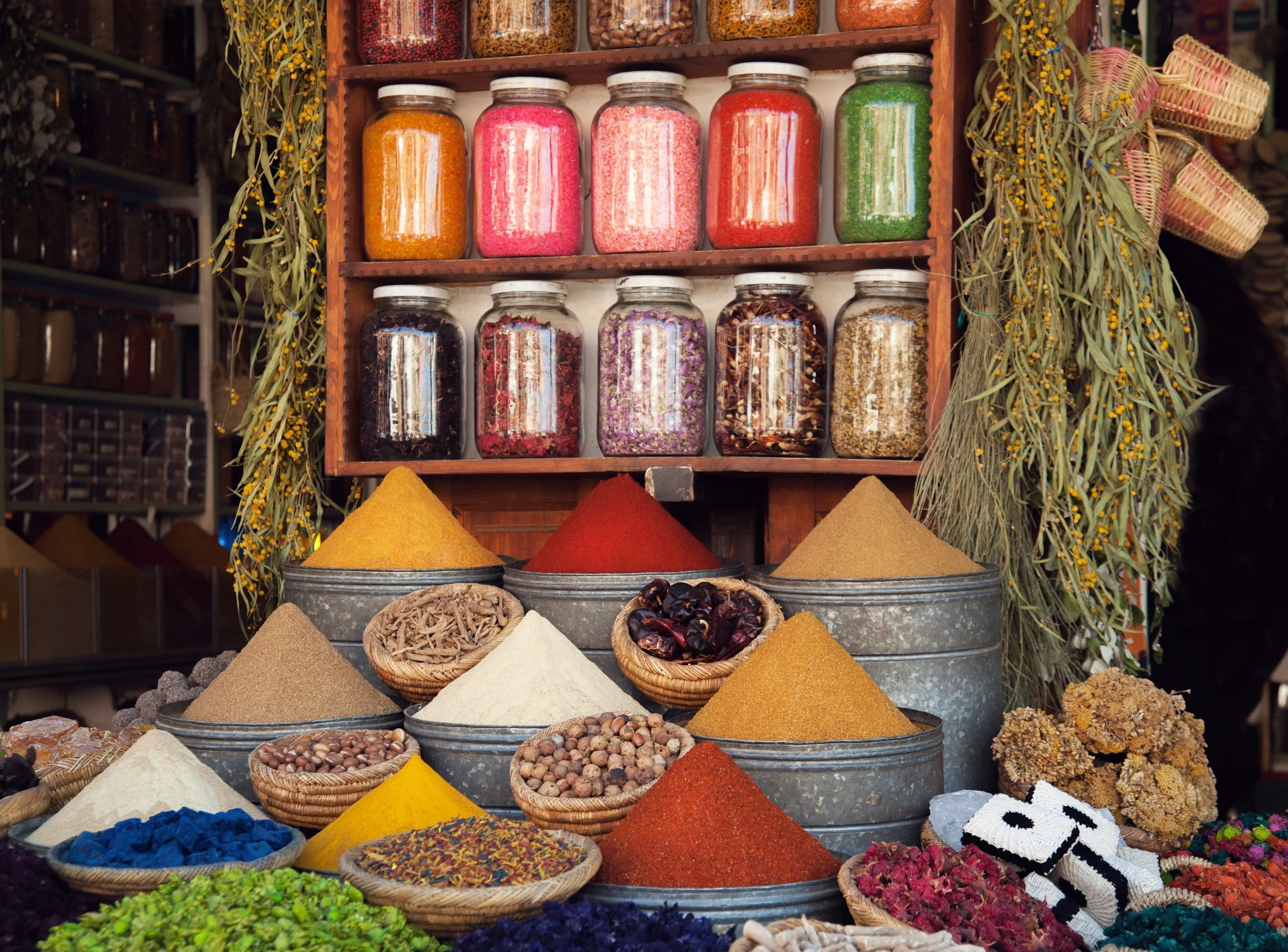 Display of various spices and herbs in jars and bowls at a market.