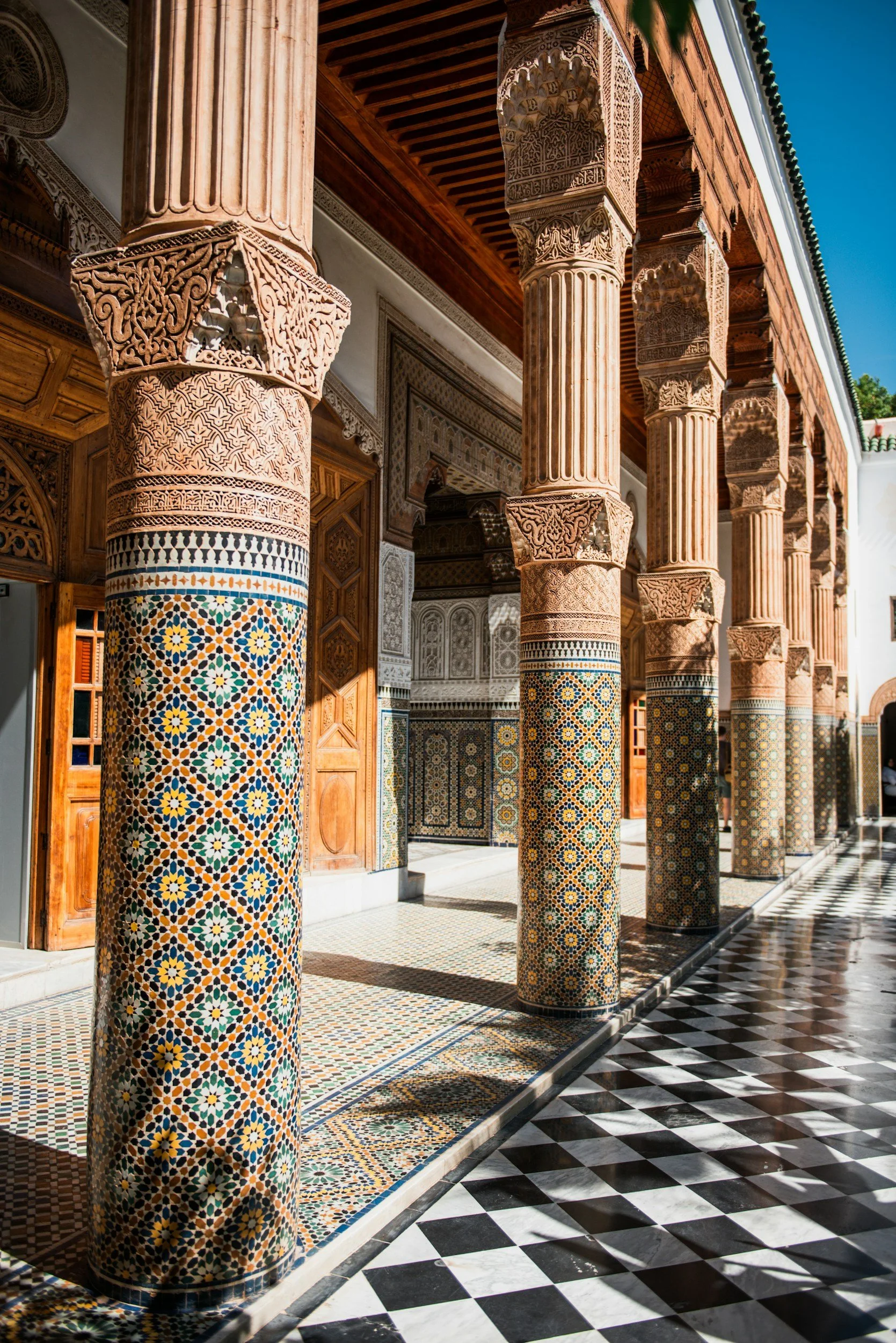 View of intricately decorated columns and arches in a Moroccan-style building with a checkered black-and-white marble floor.