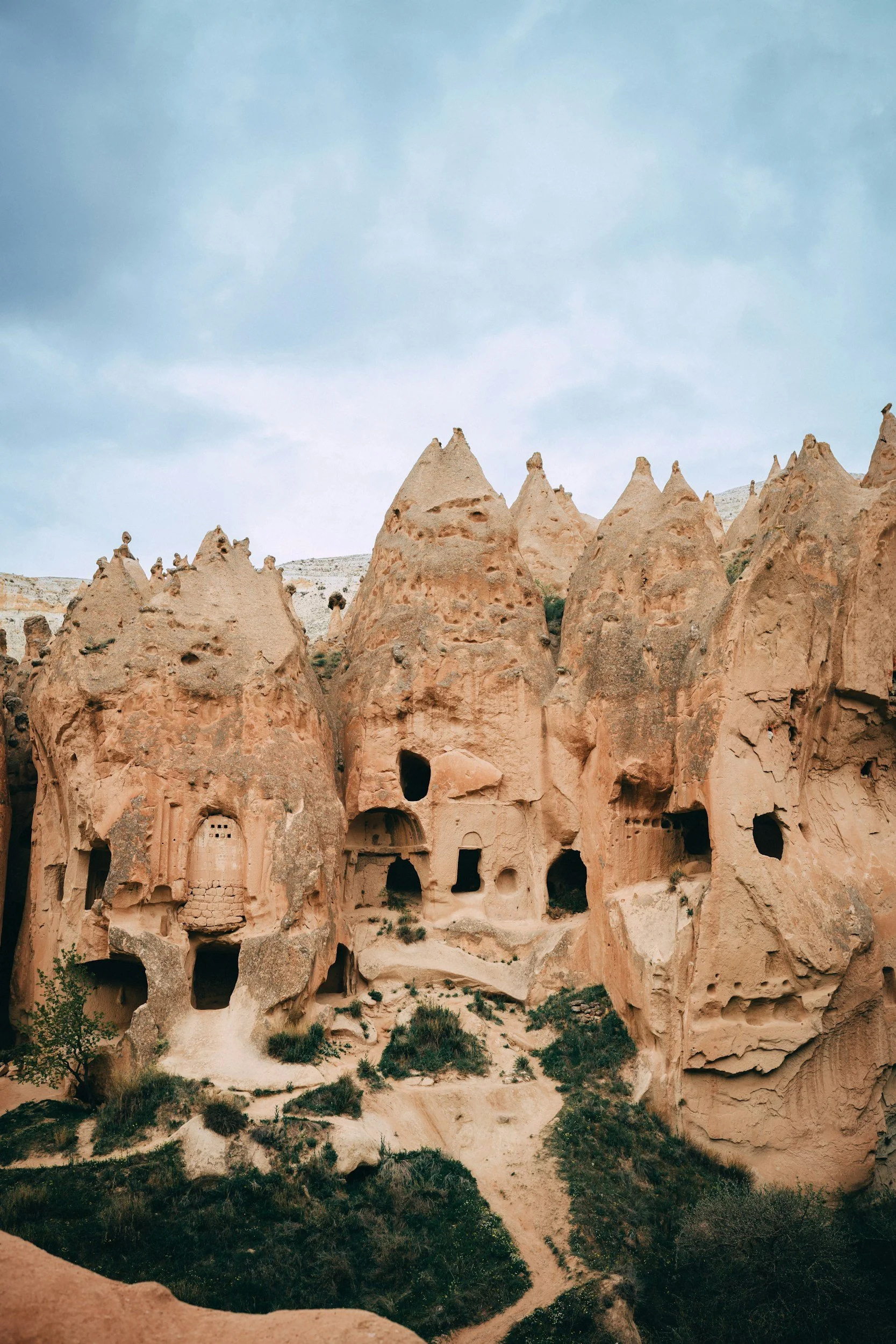 Rock formations with carved dwellings in a desert landscape under a cloudy sky.