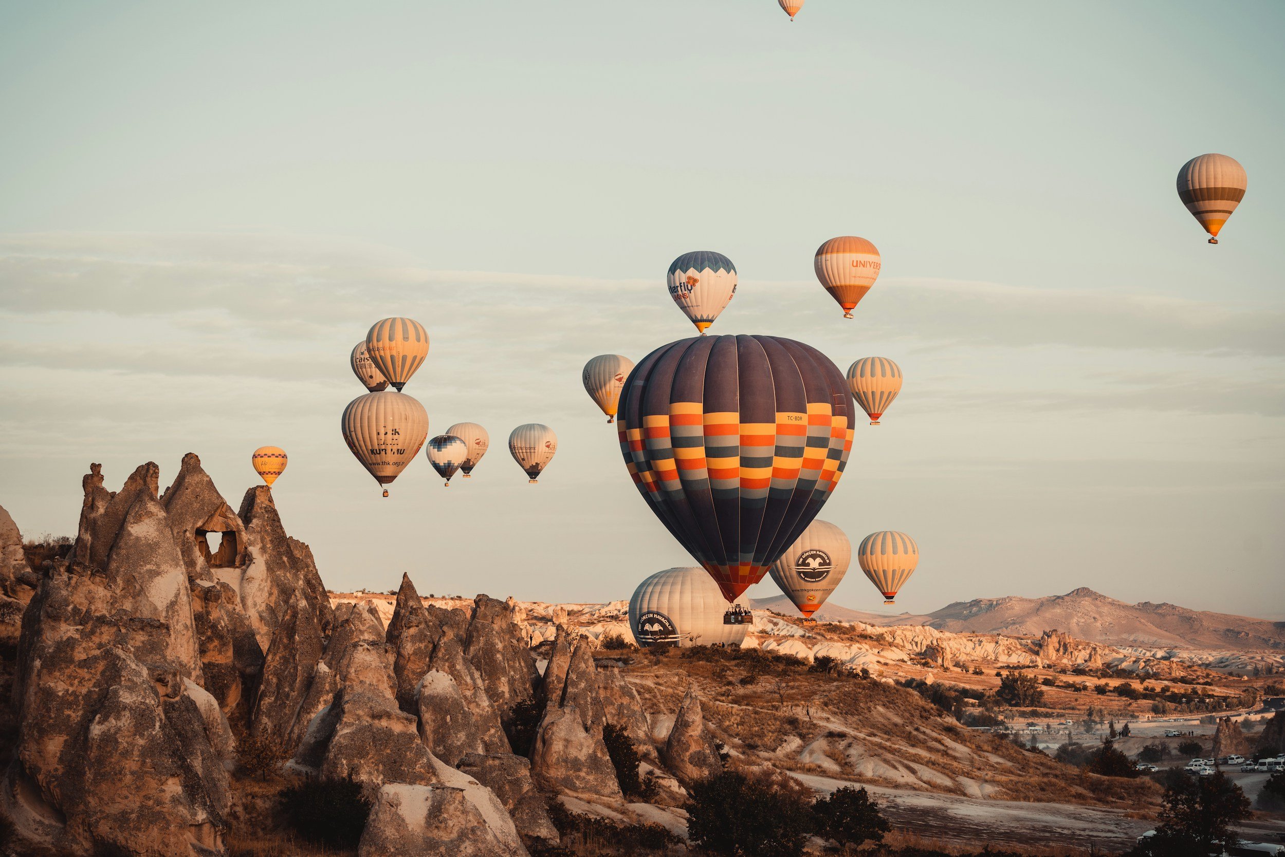 Multiple hot air balloons floating over the rocky landscape of Cappadocia, Turkey, during sunrise or sunset.