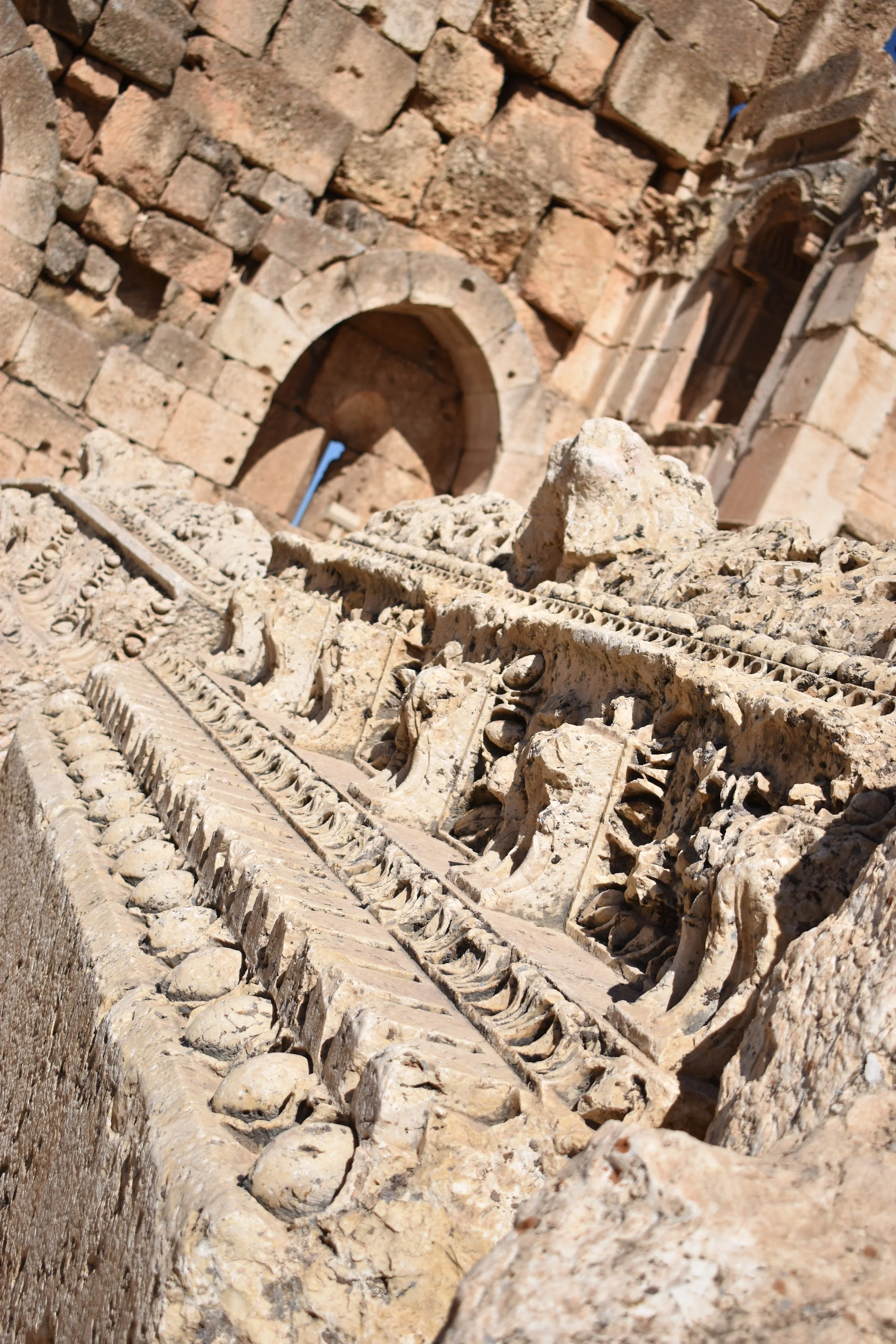 Ancient decorative stone carving with geometric patterns and figures, set against a brick wall with arches in the background.