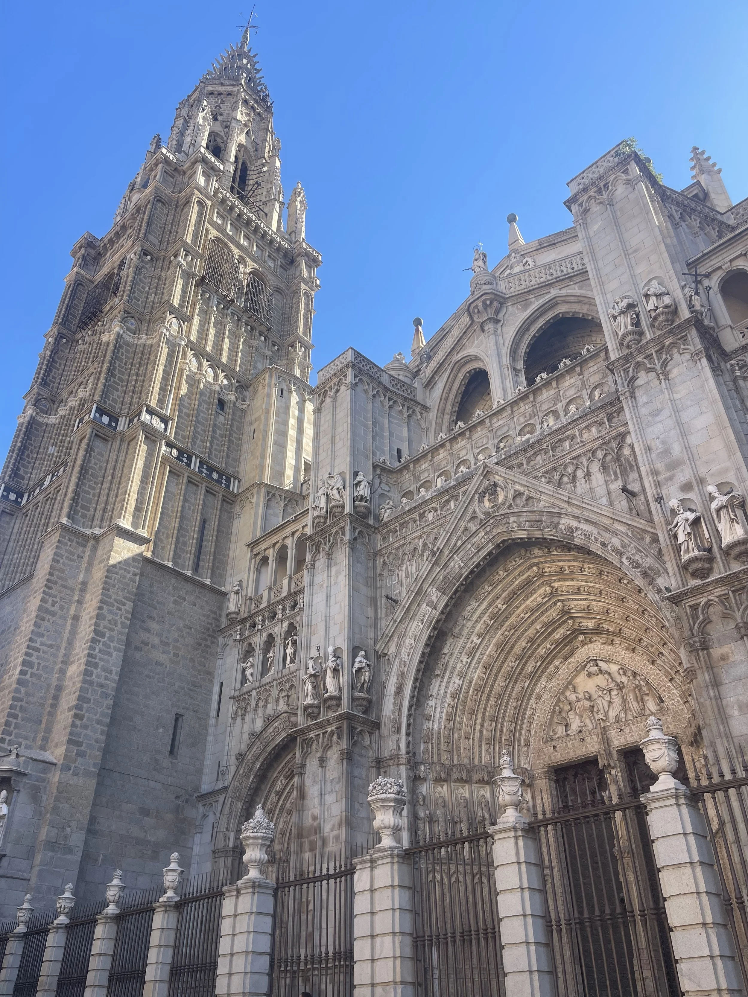 A detailed view of a Gothic cathedral with ornate stone carvings, statues, and a tall spire against a clear blue sky.