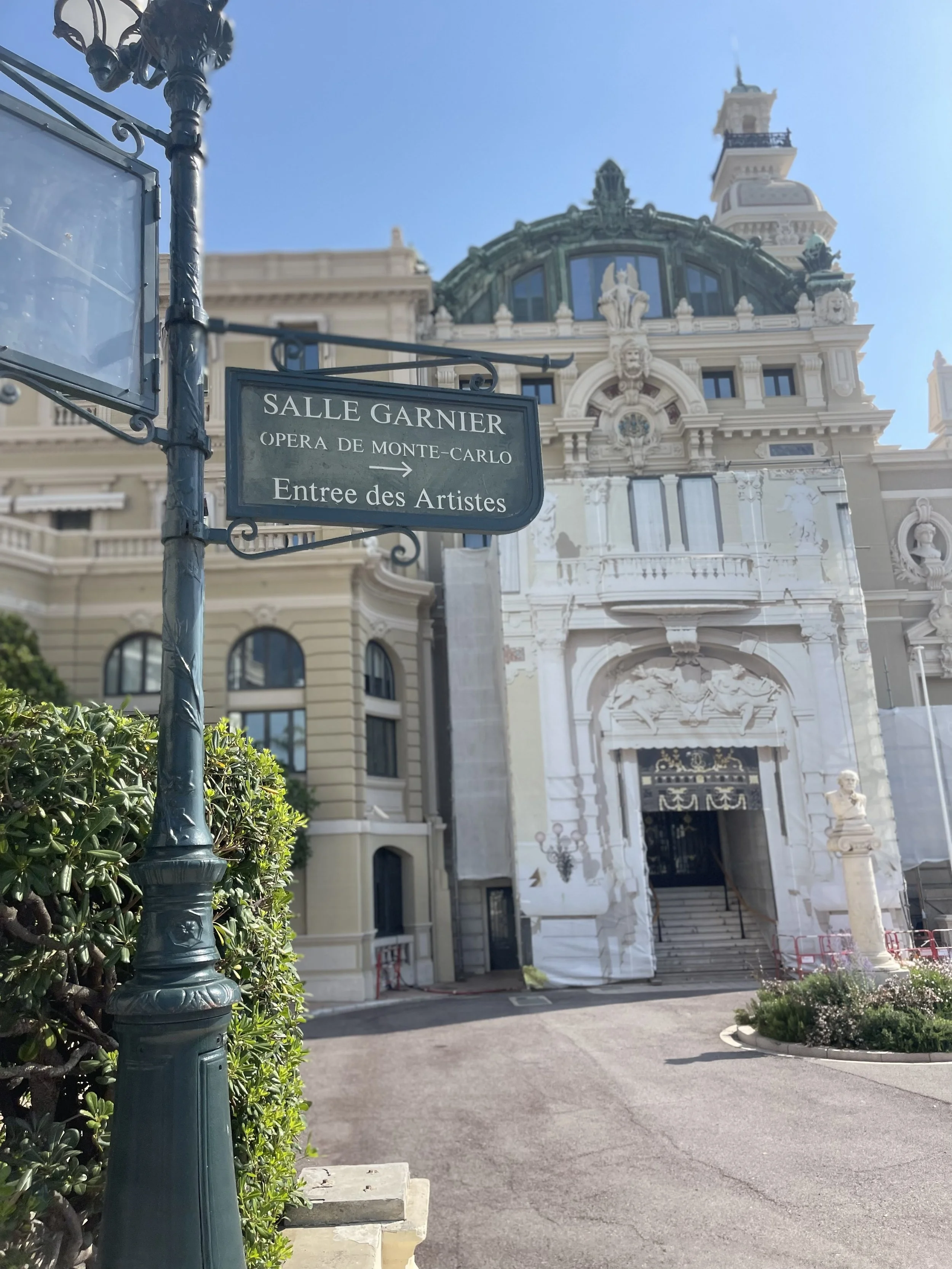 Street view of the historic Palais Garnier opera house in Monte Carlo, Monaco, with a sign pointing to the entrance for artists.