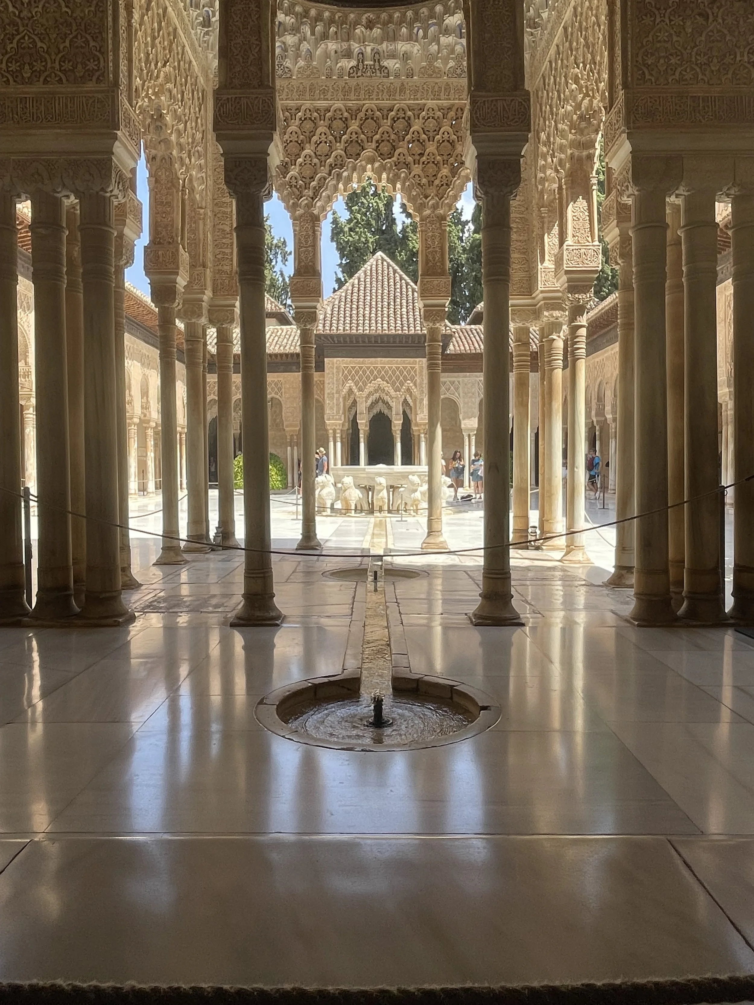 Interior courtyard with ornate arches, columns, and intricate architectural details, featuring a small fountain and visitors exploring the area.