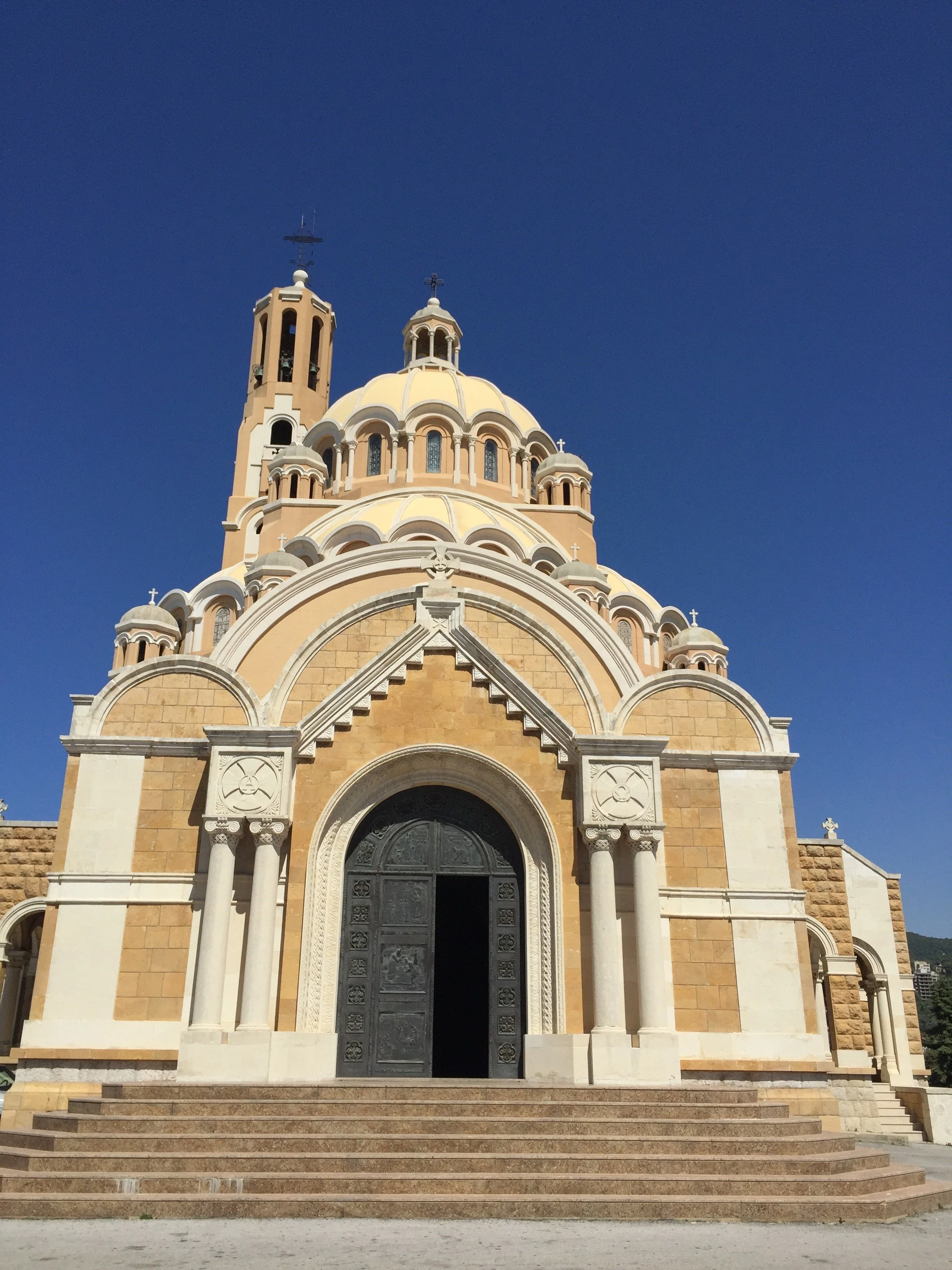 A large church with a domed roof, ornate columns, and steps leading up to a detailed door, under a clear blue sky.