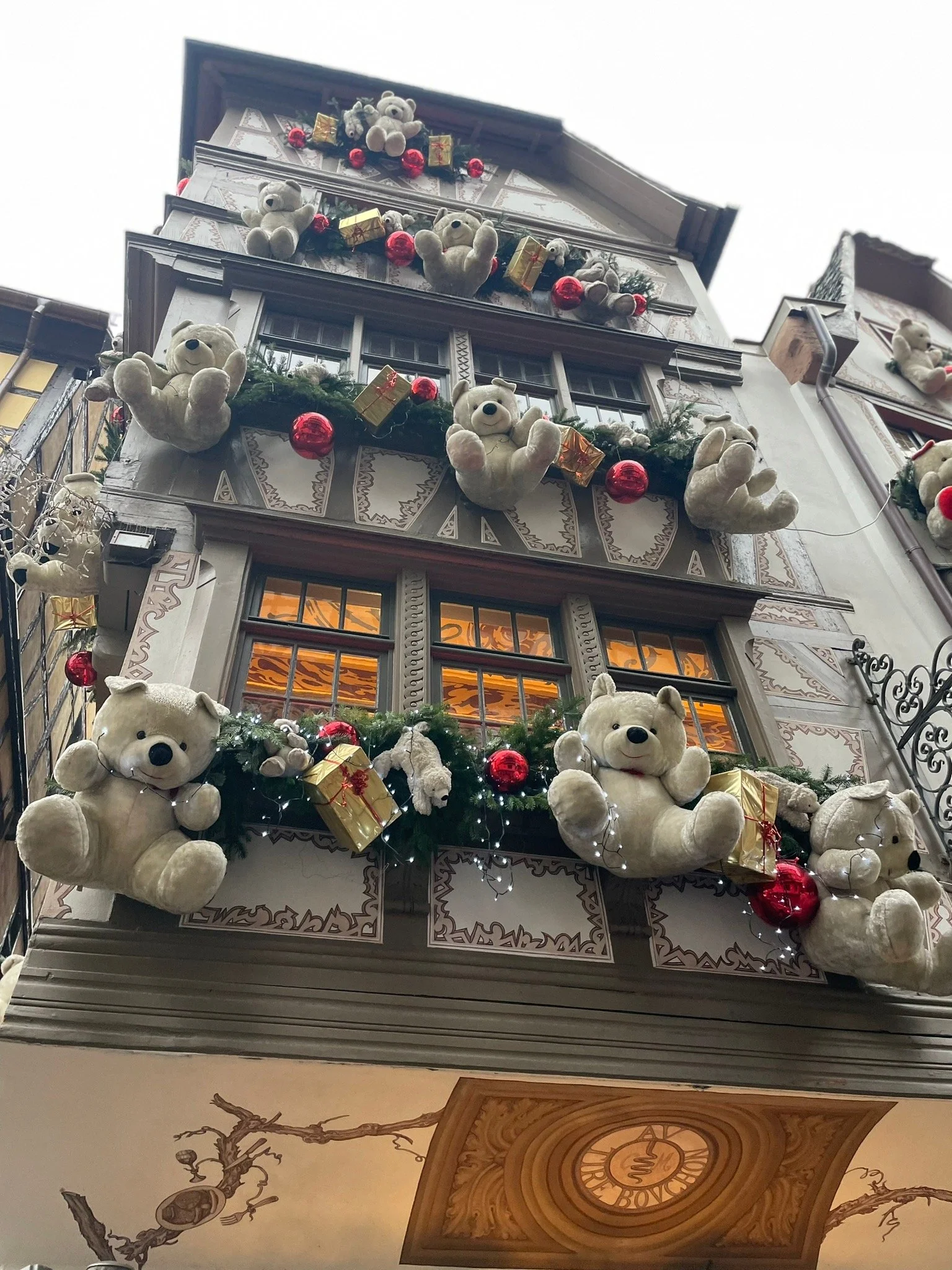 Festive building decorated with plush teddy bears, Christmas ornaments, red baubles, gold gift boxes, and string lights.