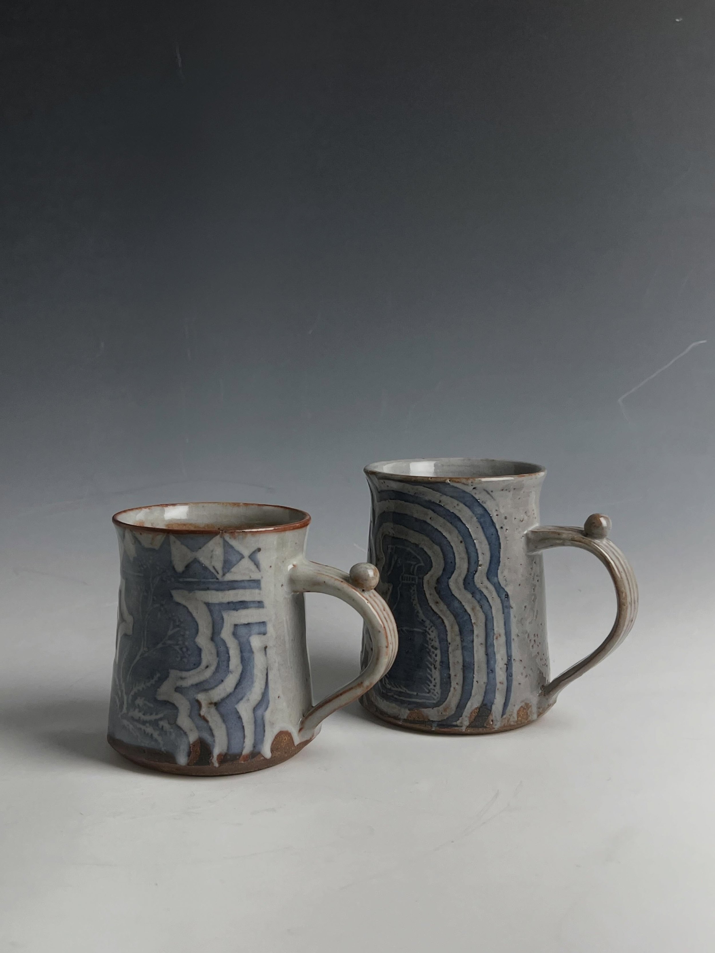 A pair of mugs made this year combining some older sgraffito techniques layered under gosu slip/ shino glazing that i have become a recent fan of. Lizella clay. I think the muted blue is kind of fun but could be punchier.