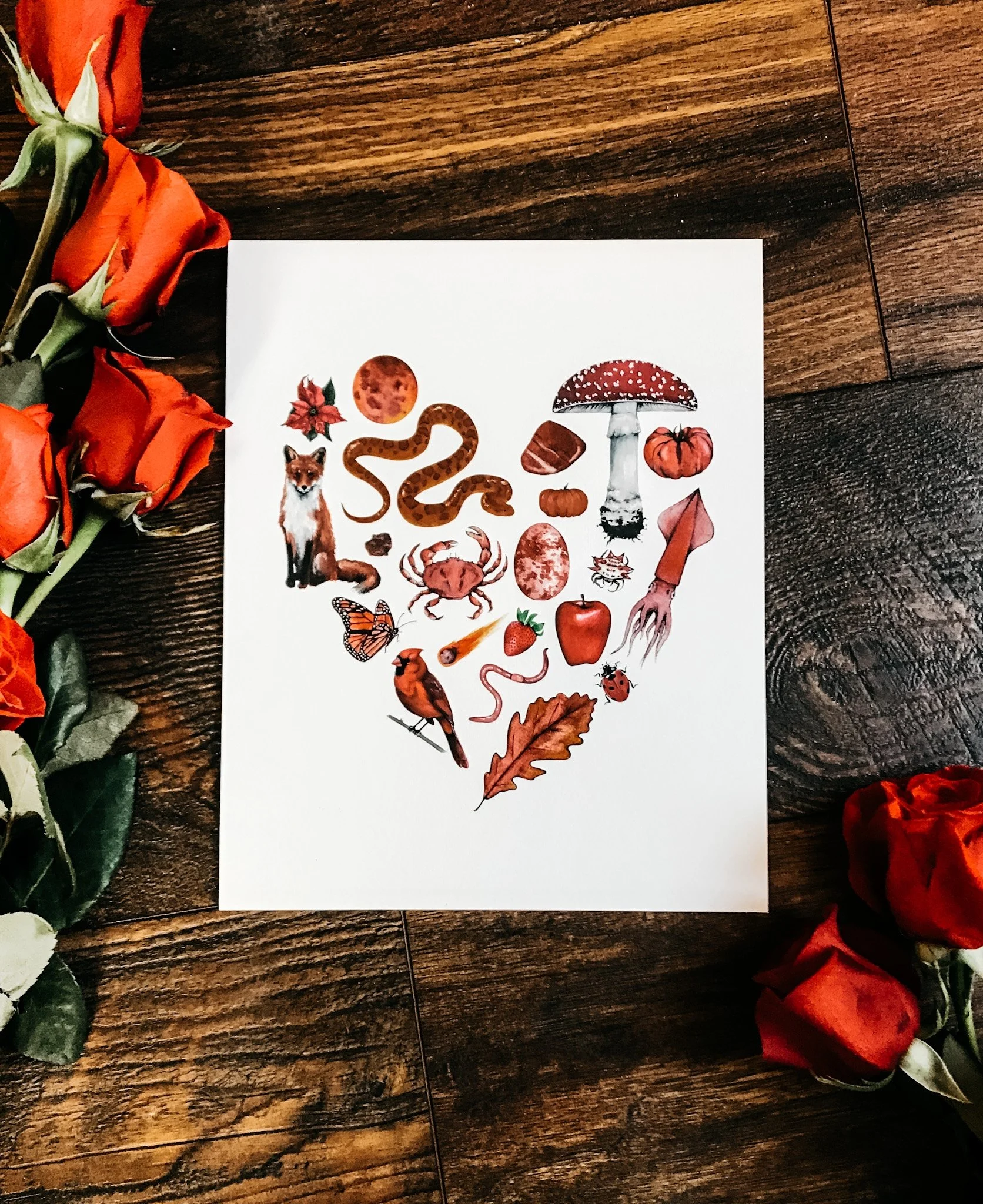 Nature-themed heart art print featuring red-colored natural objects including a tomato, apple, cardinal, fox, and squid arranged in a heart shape.