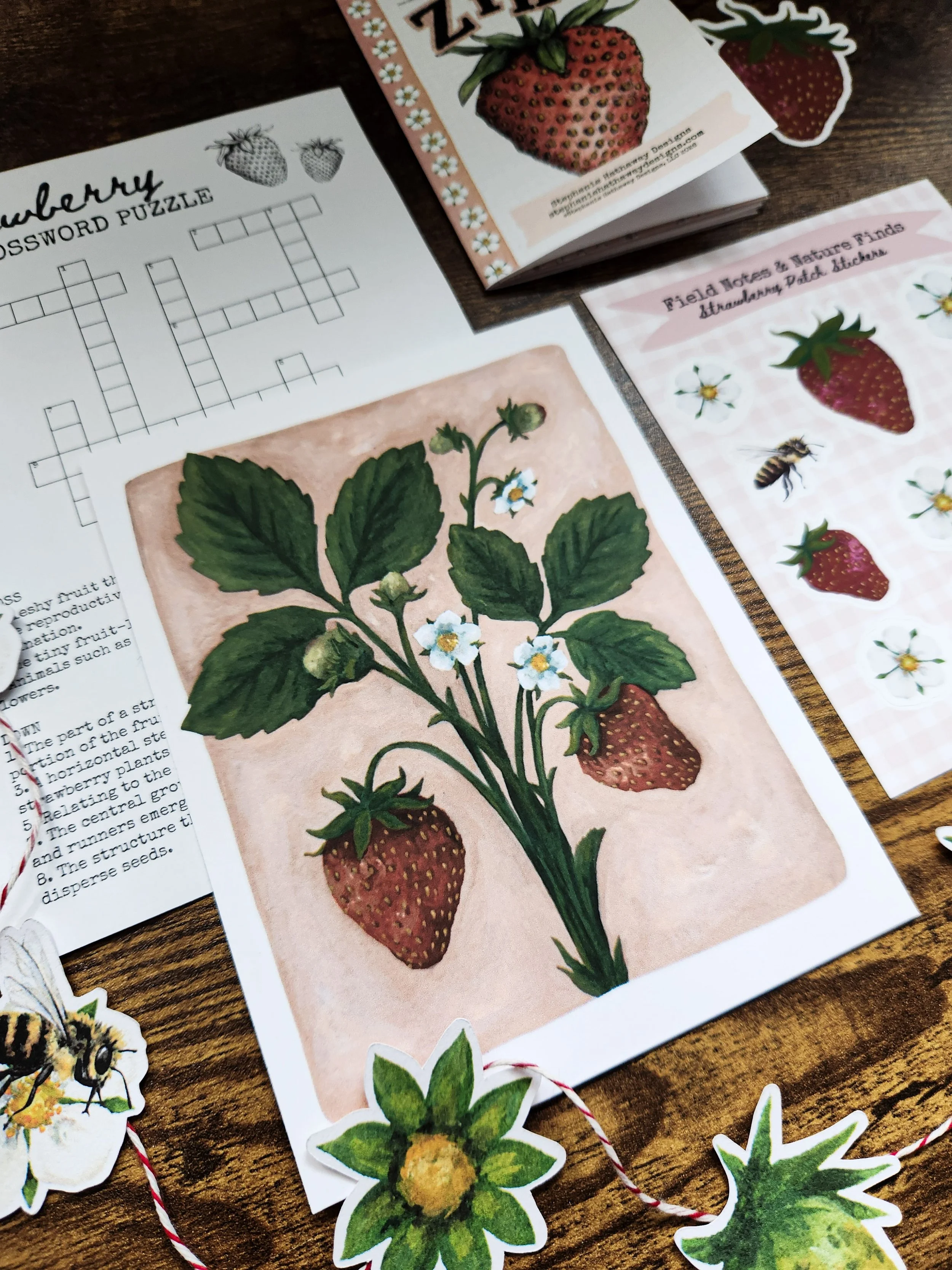 Strawberry-themed snail mail collection shown from a different angle, highlighting the art print, sticker sheet, nature zine, life cycle garland, and crossword.