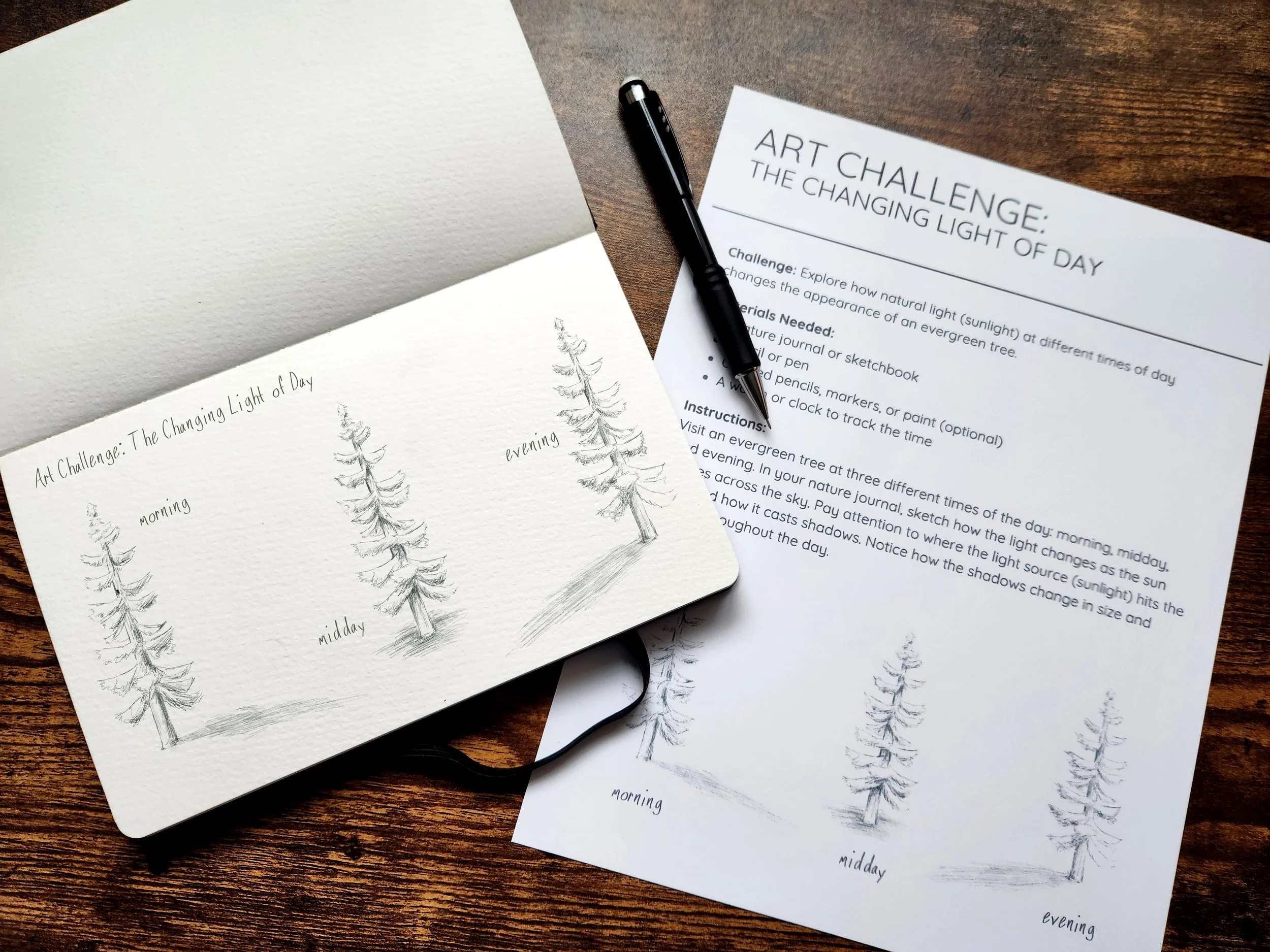 A sketchbook with pencil drawings of a pine tree at different times of the day: morning, midday, and evening. Next to it is a printed sheet titled 'Art Challenge: The Changing Light of Day' with instructions and a pen placed on top.