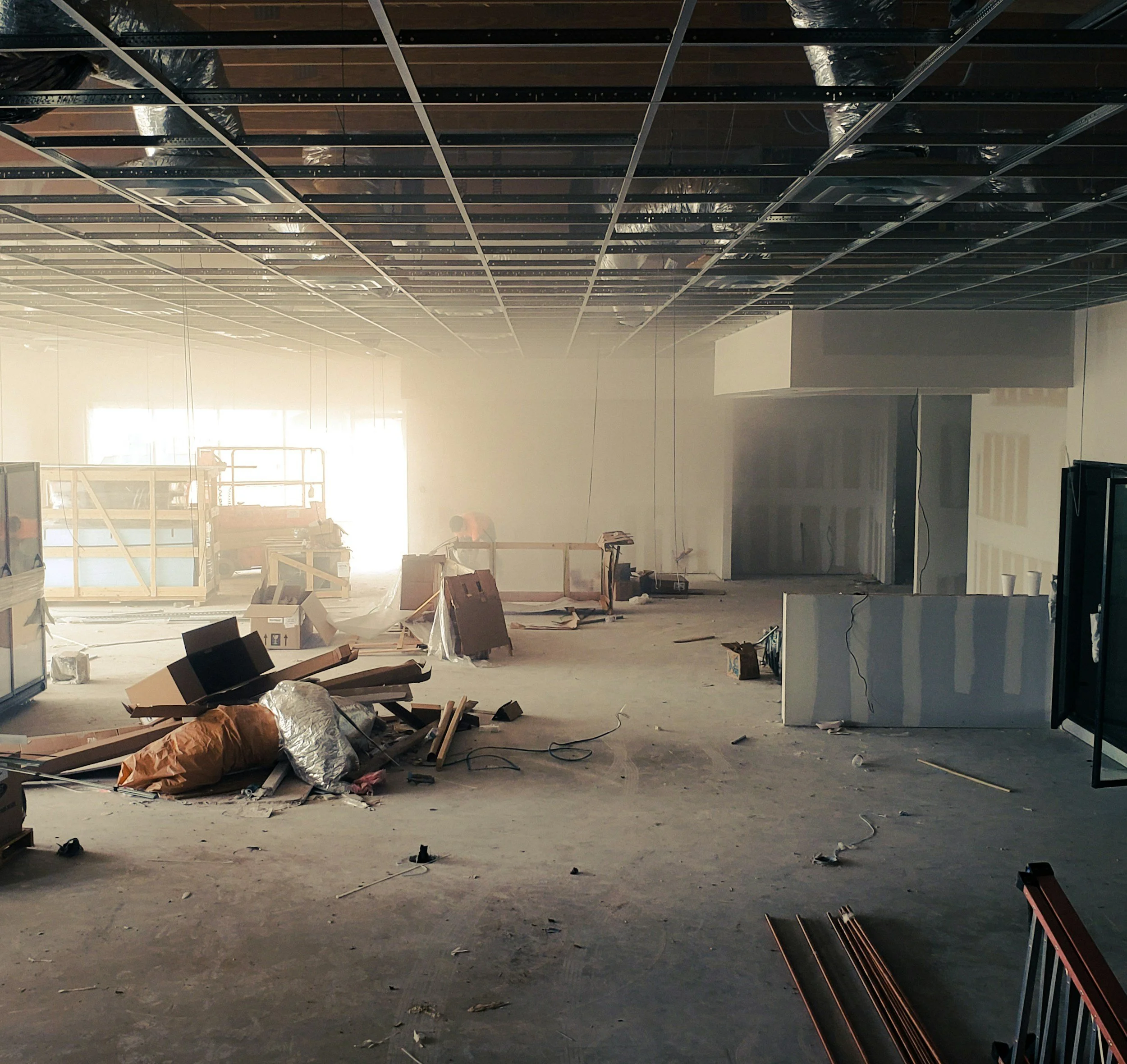 Interior of a building under construction or renovation with exposed ceiling framework, construction materials, and building debris scattered across the floor.