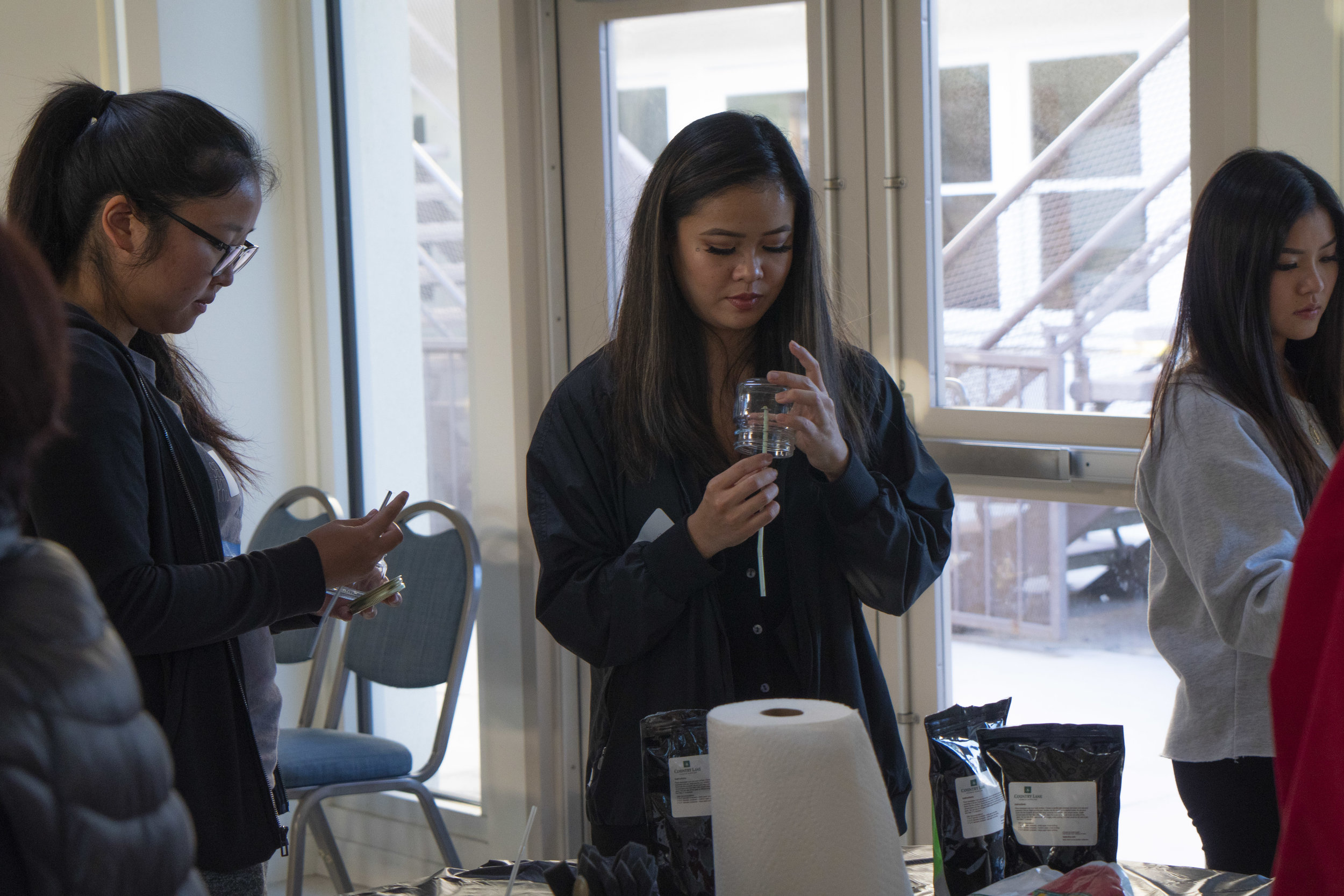 A woman with long black hair attaches a wick to the bottom of a glass.