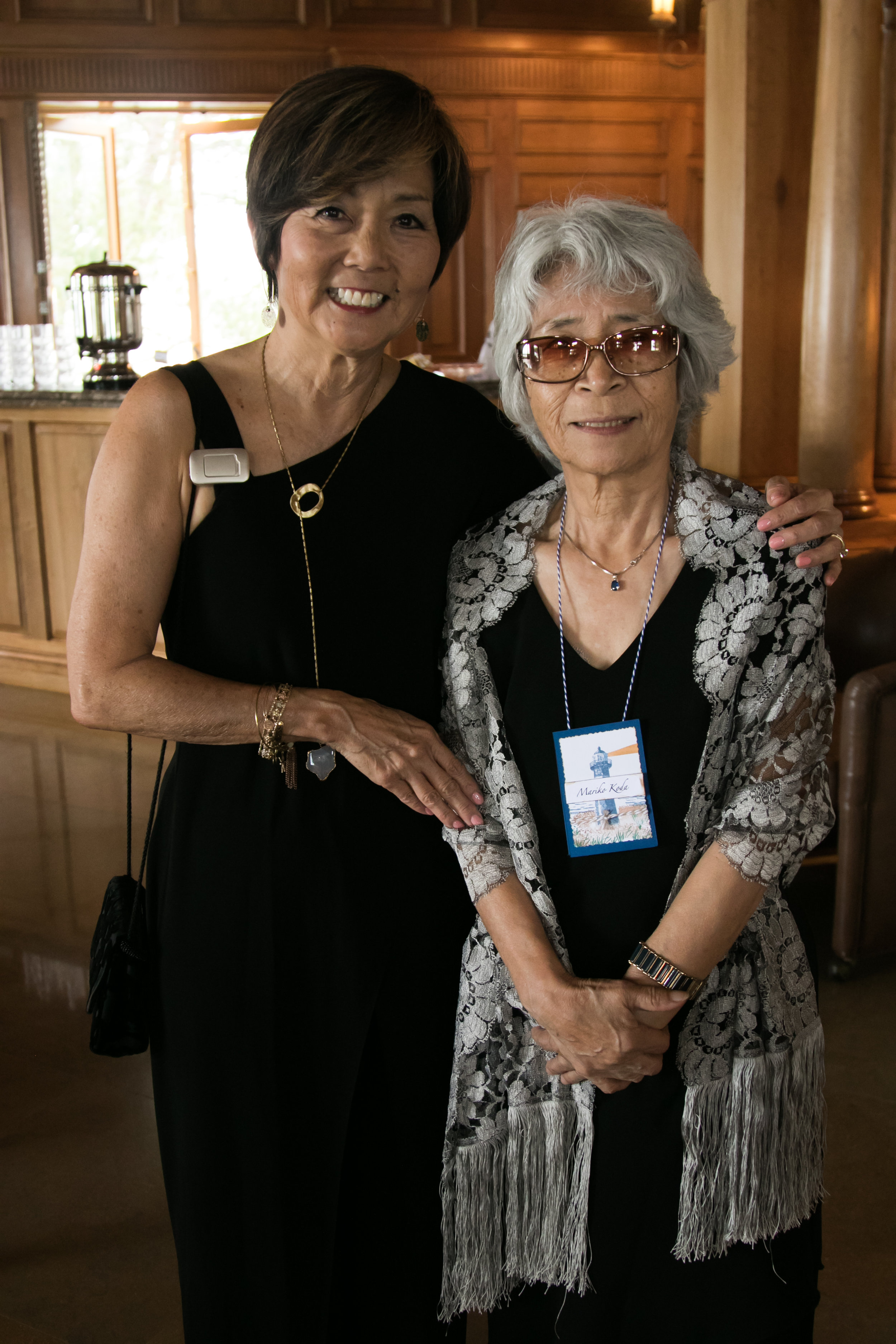 A woman with her arm around an elder woman smiles.