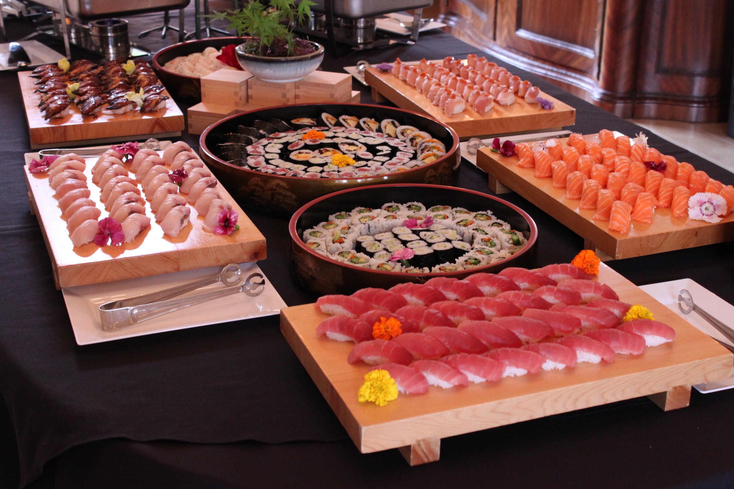 Eight platters of various sushi rests on a table. 