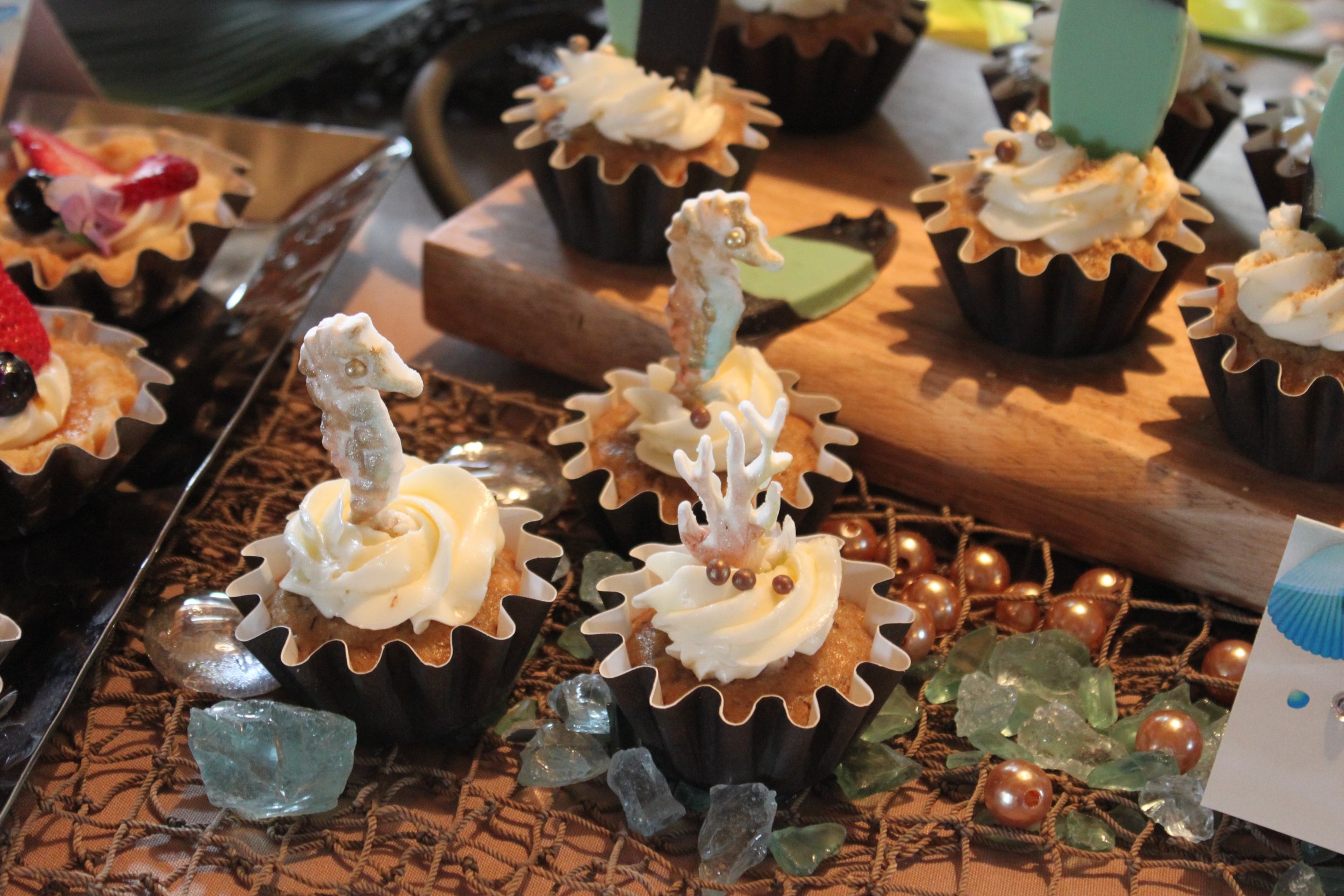 Cupcakes decorated with seahorses and coral are surrounded by rocks on a table. 