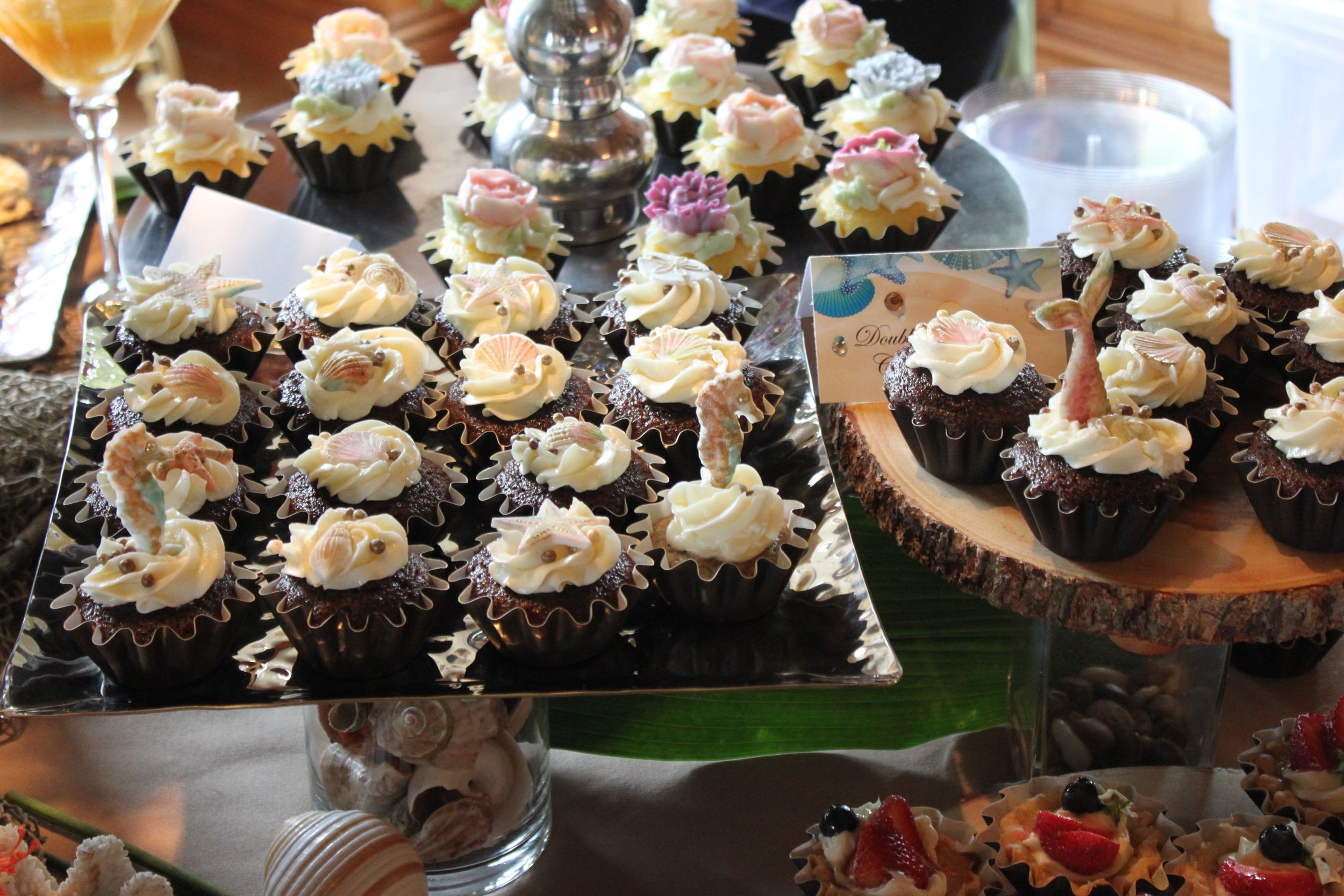 Cupcakes decorated with seahorses, mermaid tails and flowers rest on the table. 