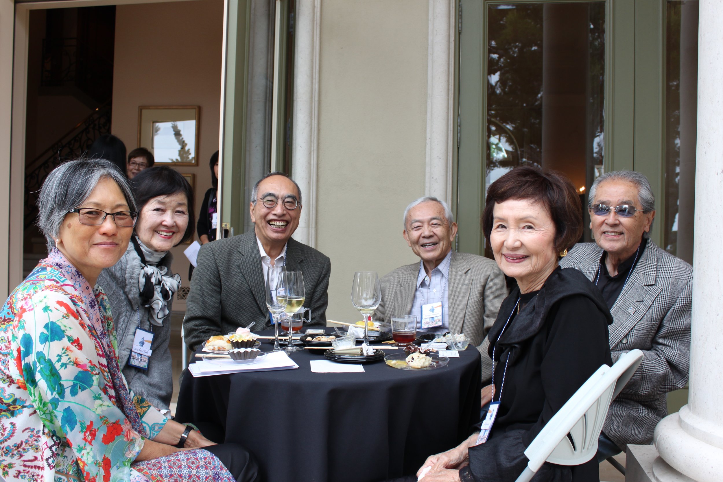 A group of Asian older men and women smile while seated at a round table together. 