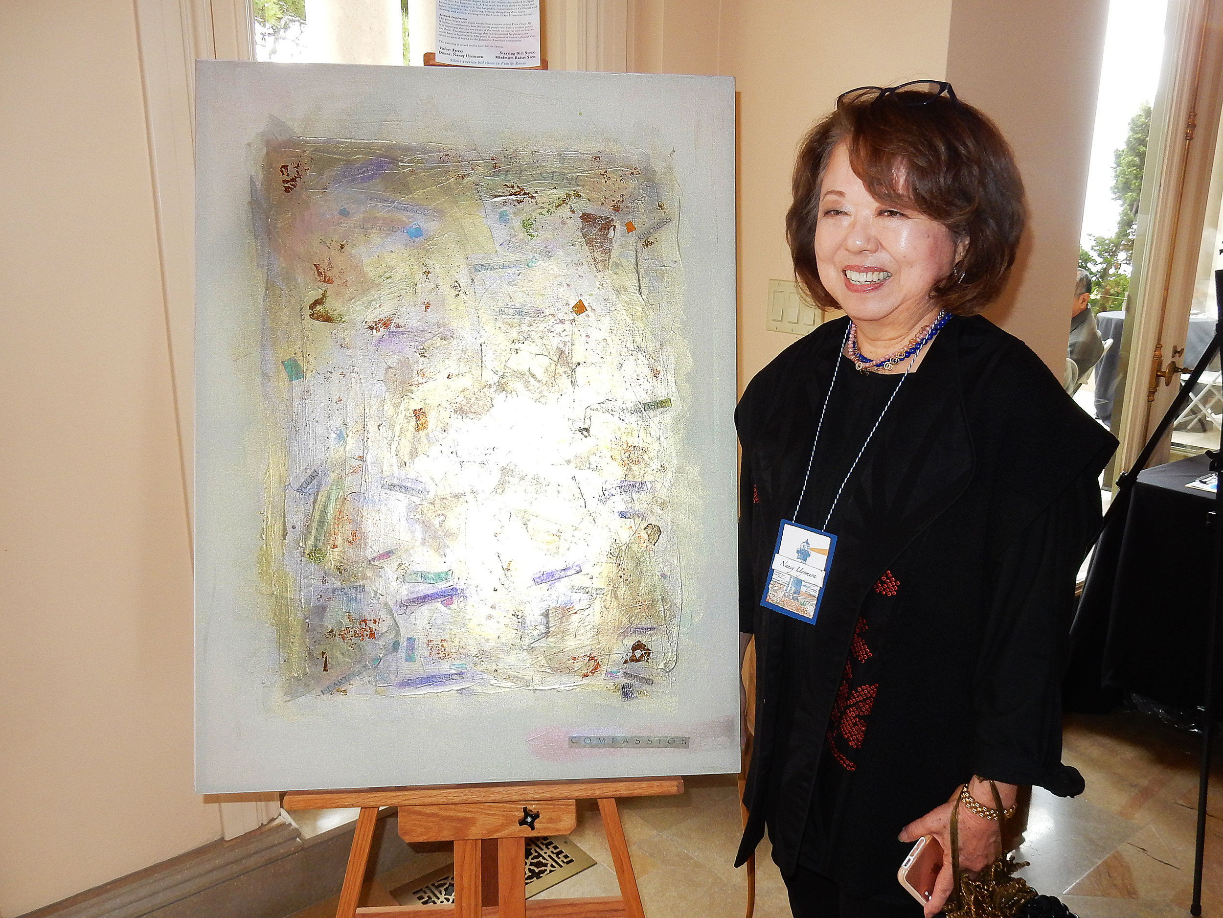 A woman smiles while standing next to a large painting. 