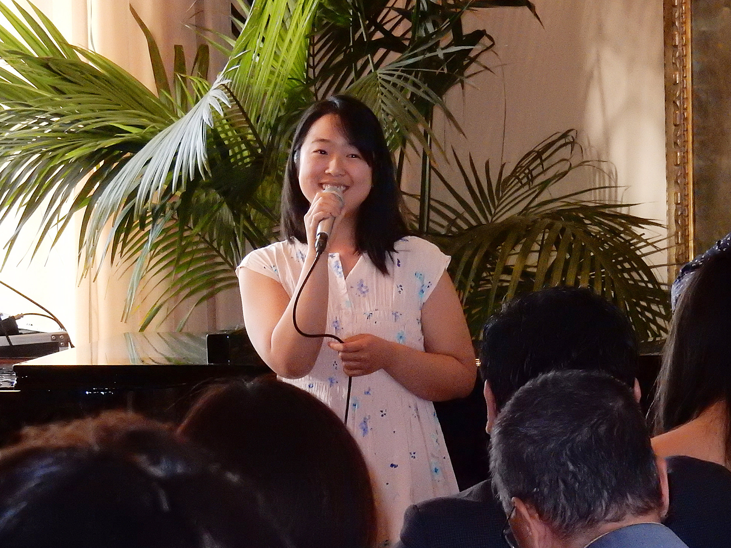 A woman with a microphone speaks to a group inside. 