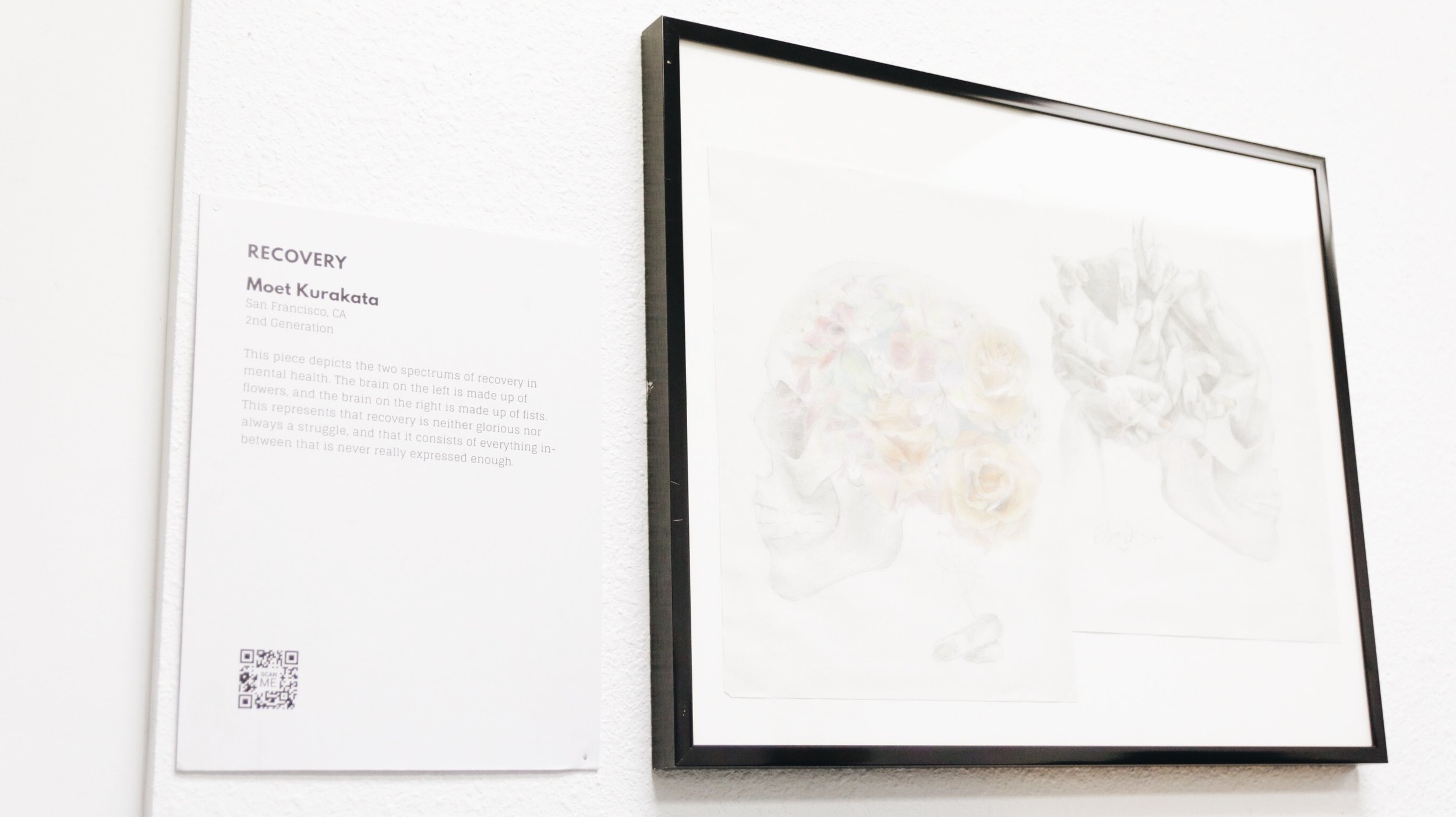 The art piece “Recovery” by Moet Kurakata hangs framed on a wall with a description next to it. 