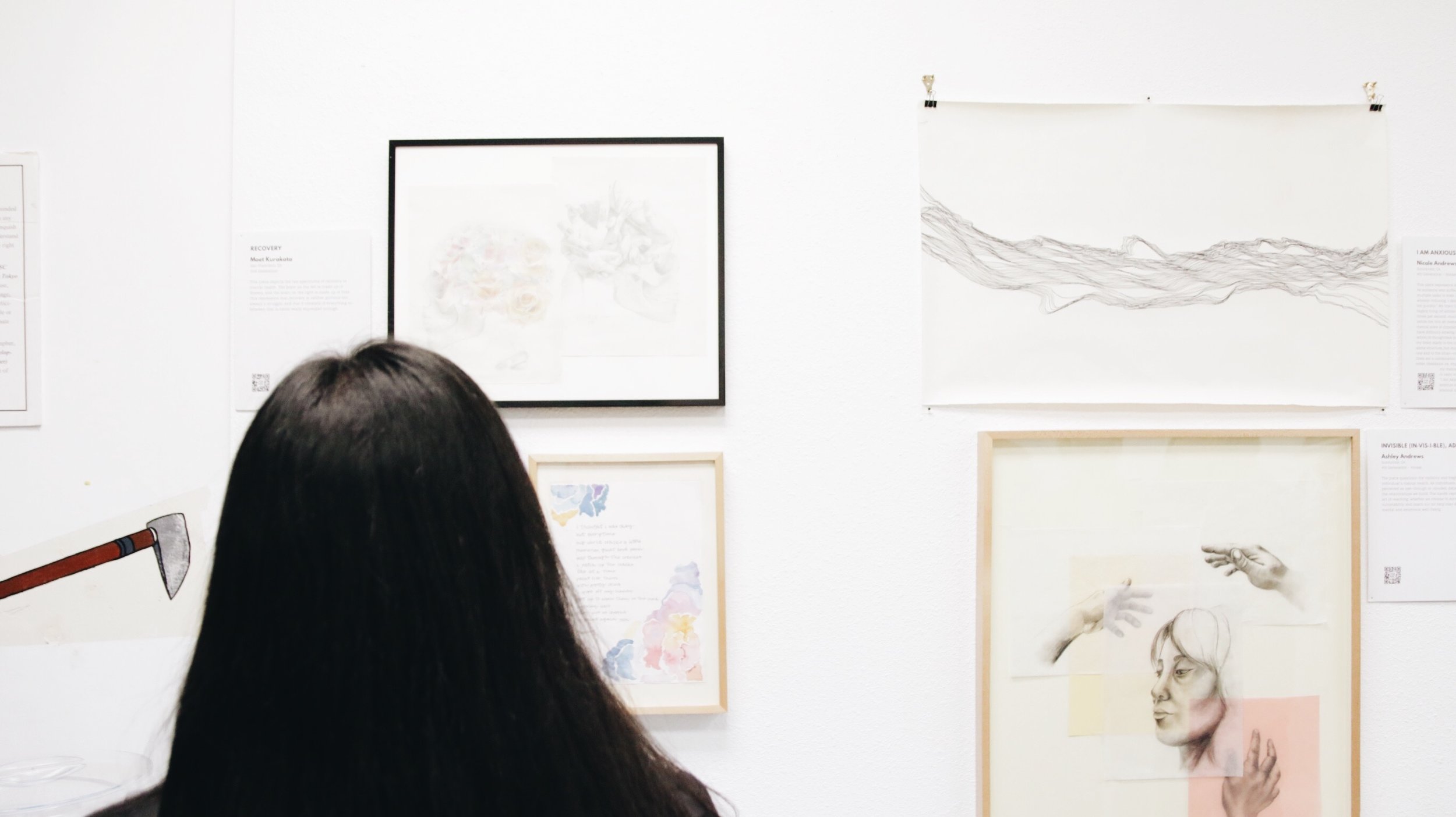 A person looks at art working hanging on the wall.