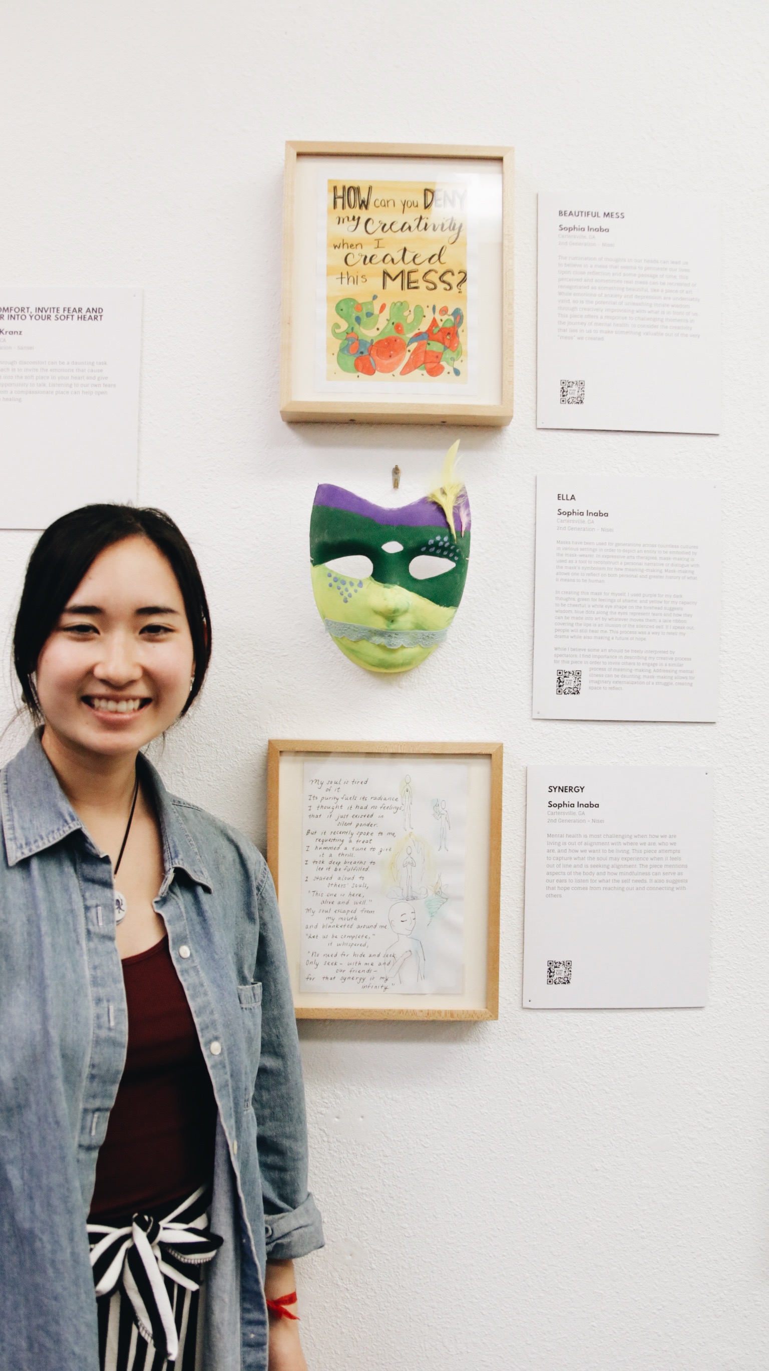 A woman poses next to a mask, called “Ella” and illustrated text, called “Synergy,” by Sophia Inaba.