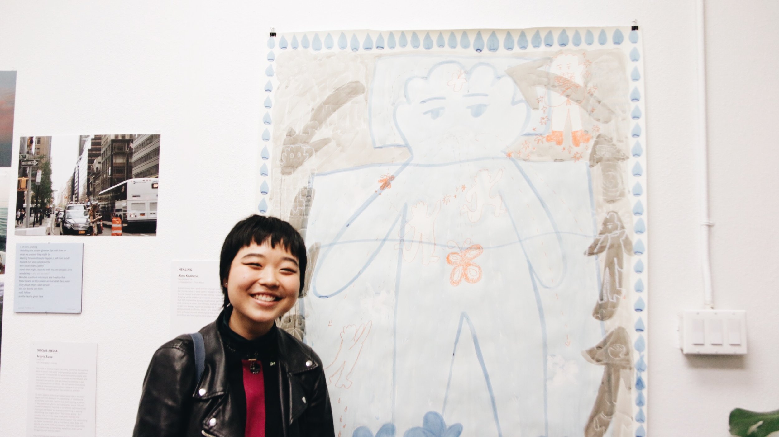 A woman smiles next to a large piece of art work on a wall. 