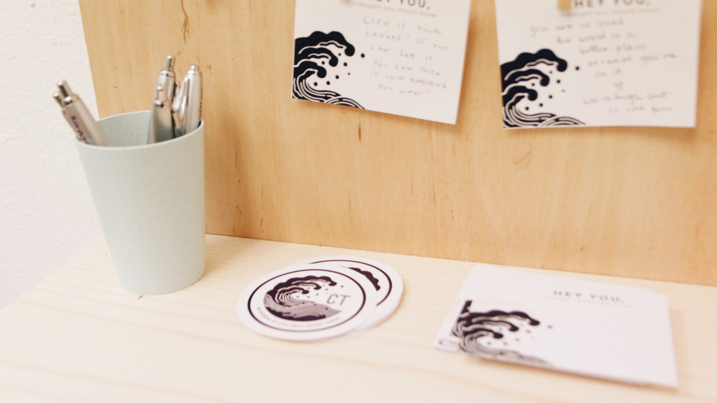 Stickers and stationary with a wave logo on it rest next to a cup of pens.