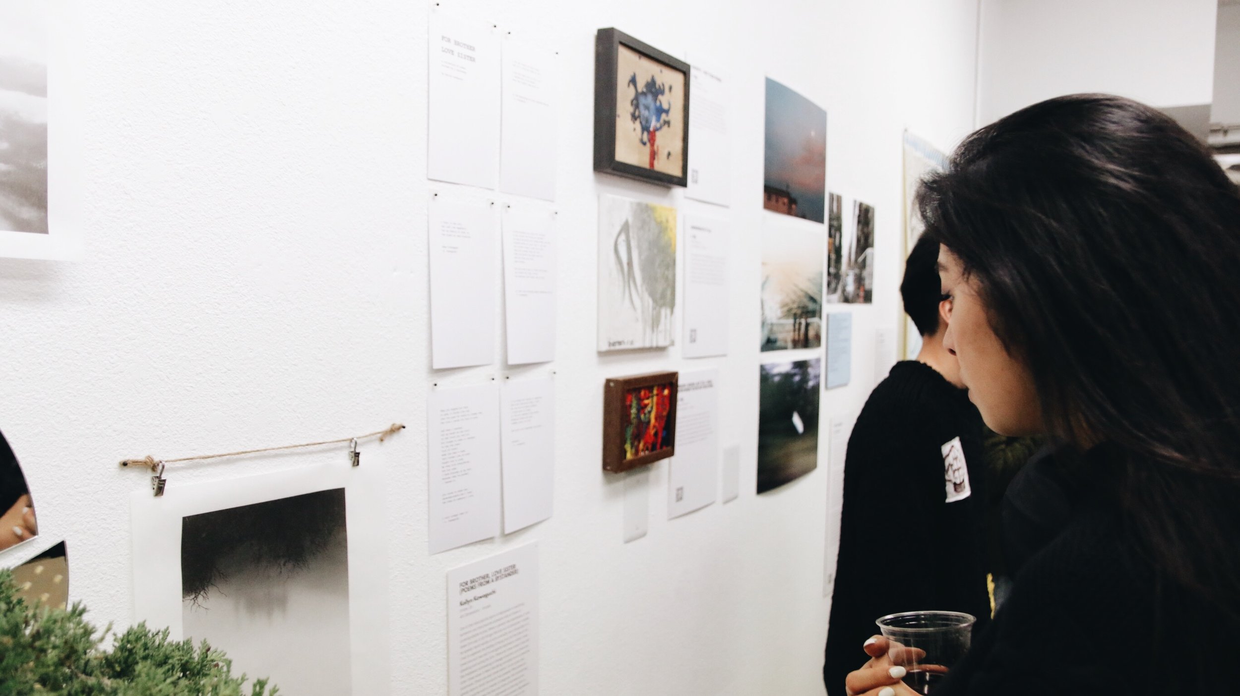 A woman holding a glass looks at art on the wall. 