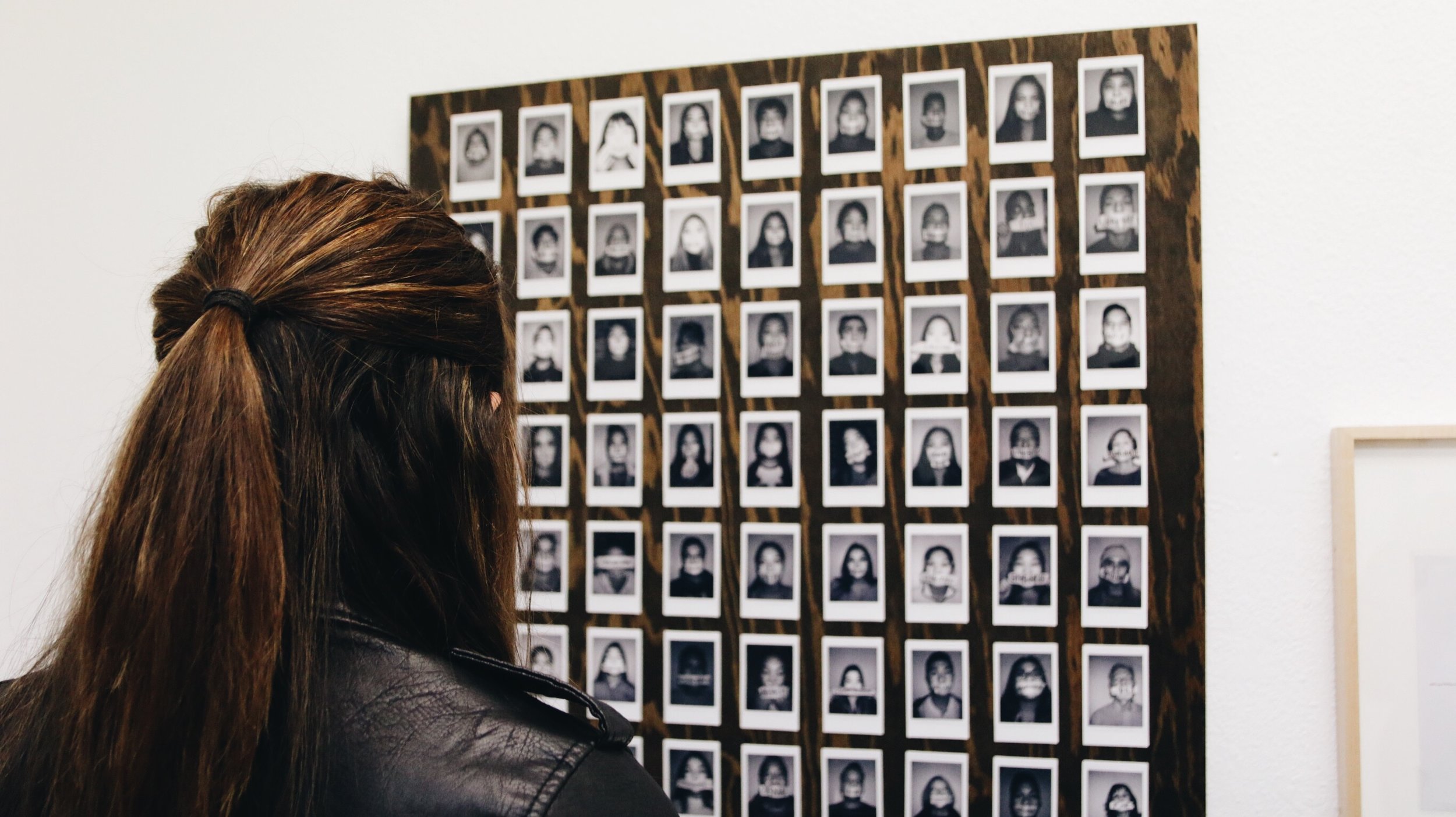 A woman looks at a series of polaroid headshots displayed as an art piece.